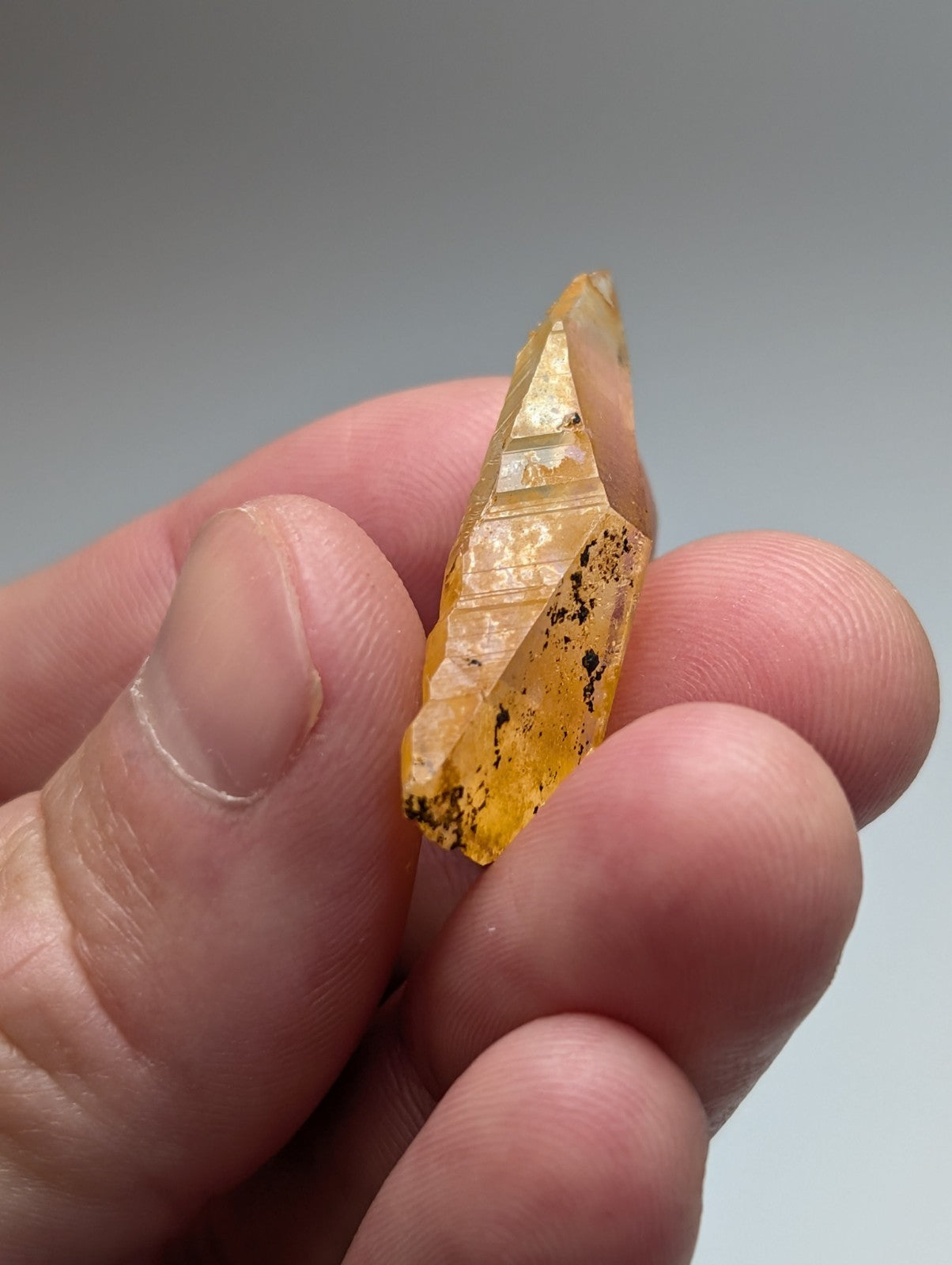 A translucent yellow arkansas quartz crystal with pointed tip and natural iridescence held gently between fingers