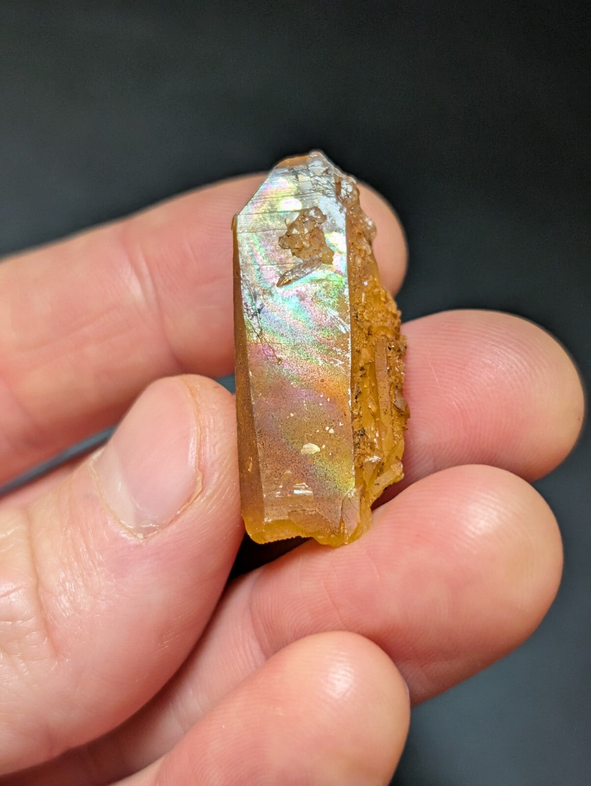 A translucent golden-yellow crystal with iridescent facets, held gently in a hand.