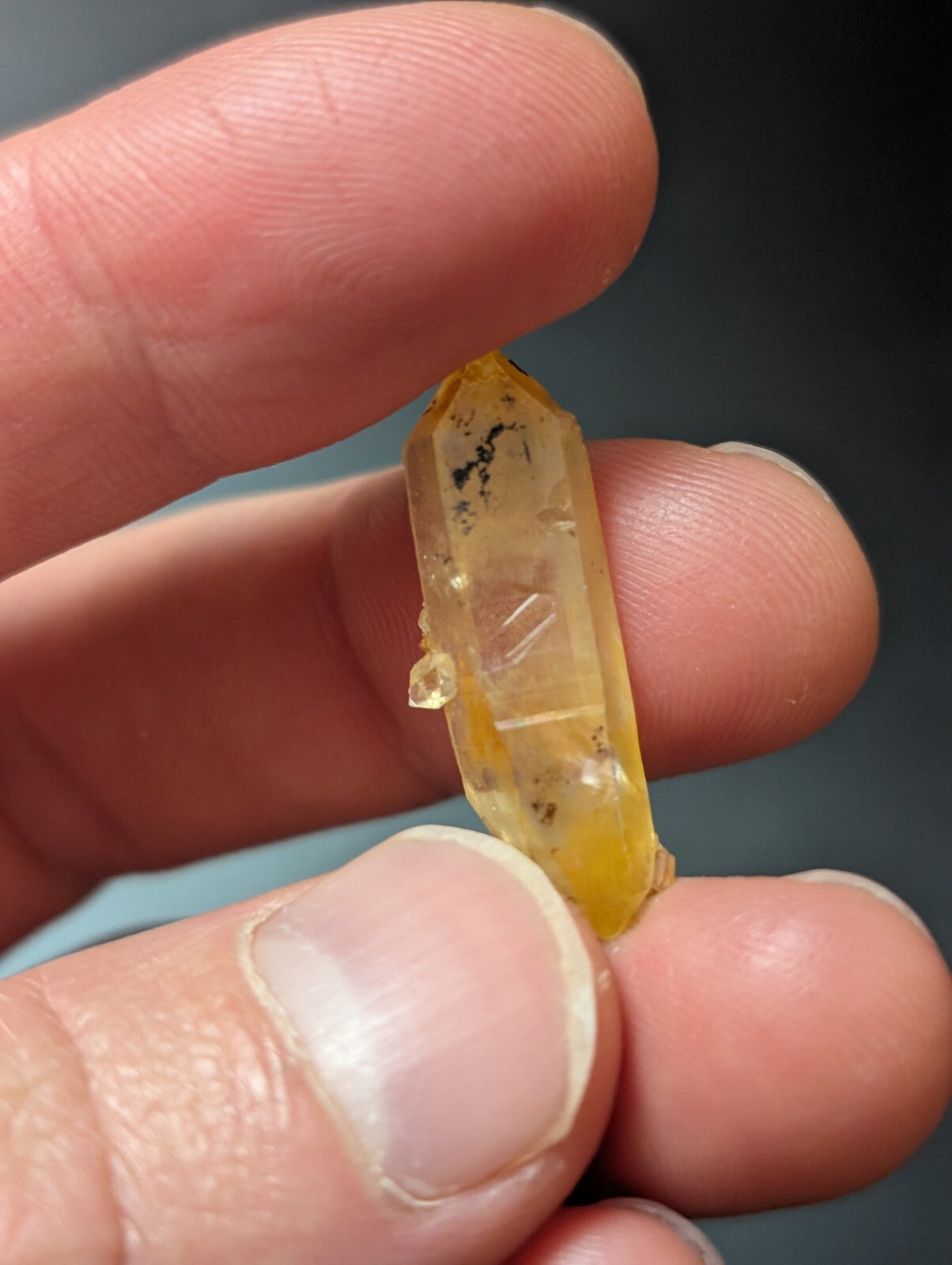 A translucent yellow crystal with natural inclusions and a pointed, faceted top.