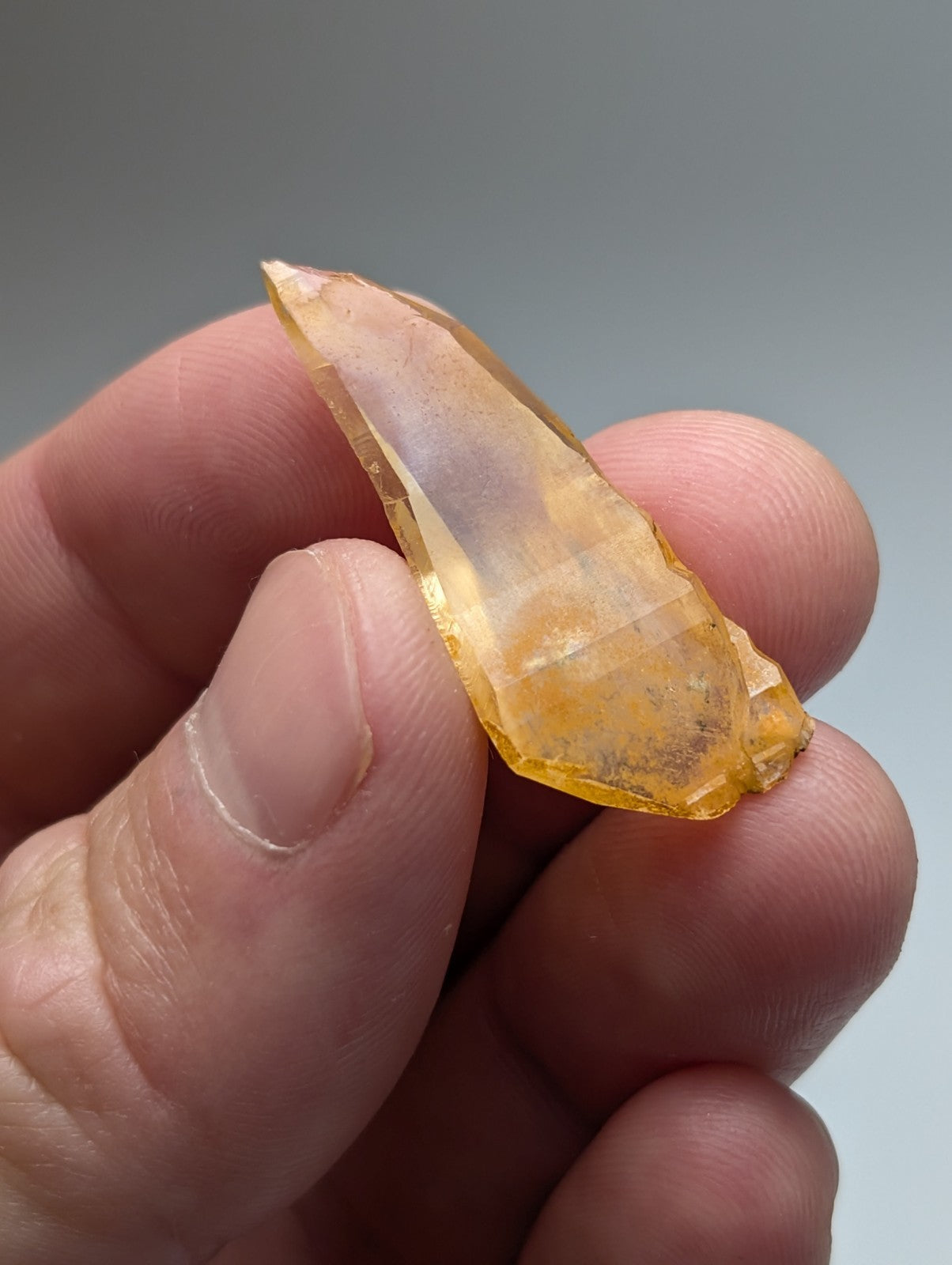 A translucent yellow arkansas quartz crystal with natural iridescence and faceted surface held between fingers