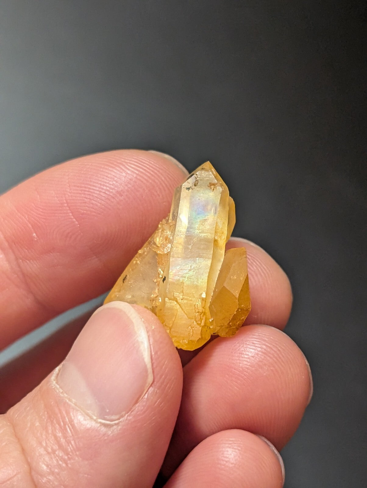 A translucent golden-yellow quartz crystal cluster with a faceted, pointed tip and subtle iridescent sheen.