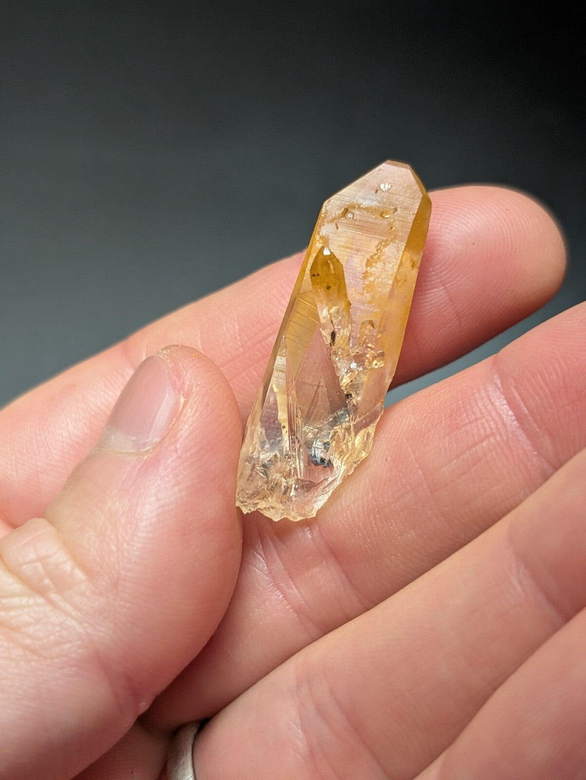 A translucent golden-yellow crystal with a pointed tip and natural inclusions, held gently in someone’s hand.