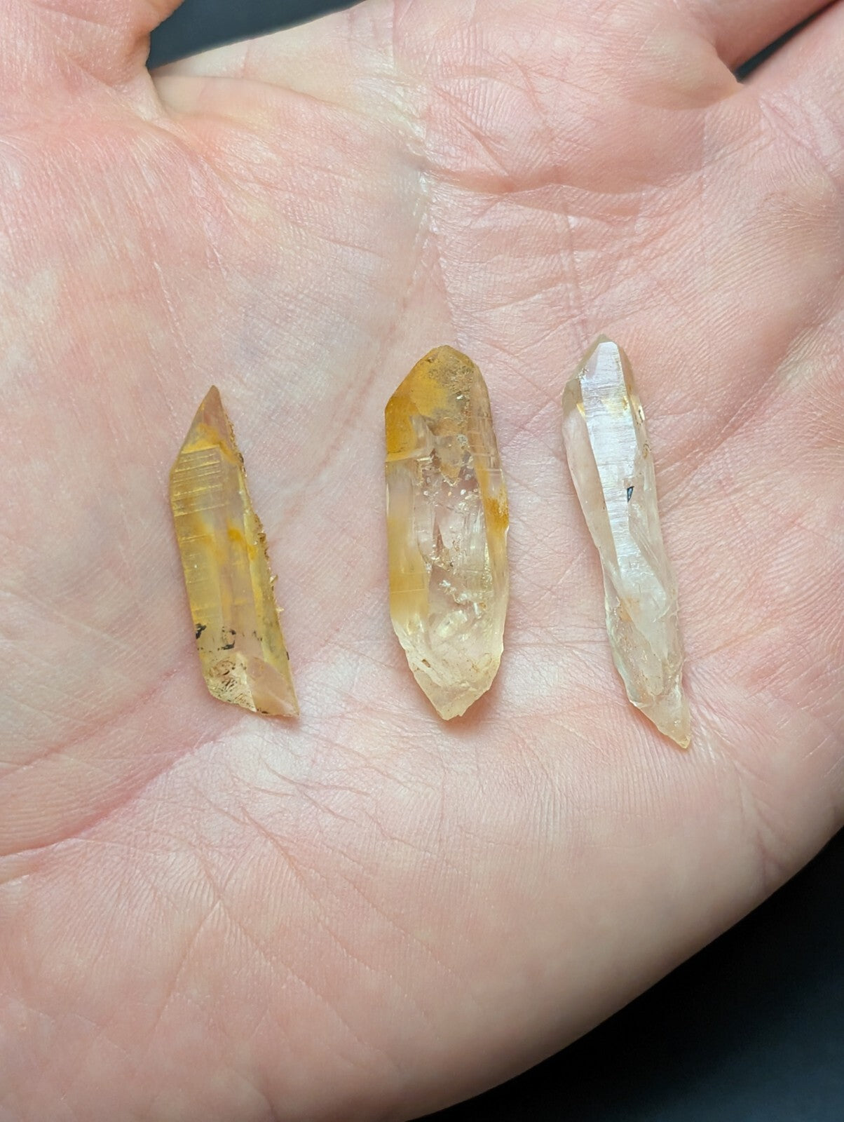 Three translucent yellowish quartz crystals with natural inclusions, held gently in an open palm.