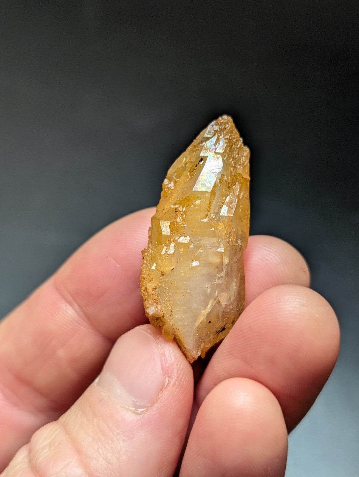 A translucent golden-yellow crystal with a pointed tip and faceted surfaces, held gently in someone’s hand.