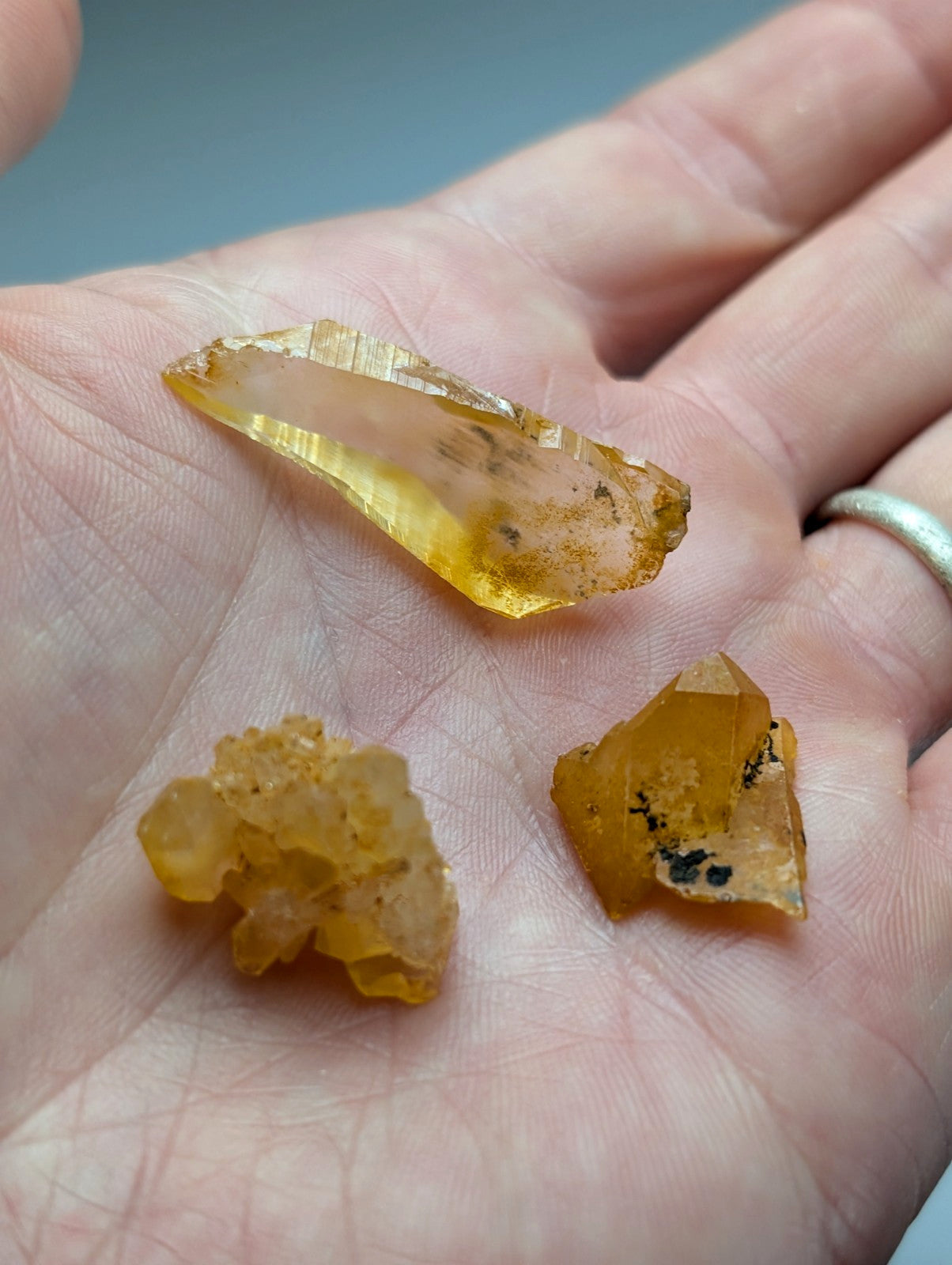 A hand holds a set of 3 golden-yellow Arkansas quartz crystals with natural iridescence and unique shapes