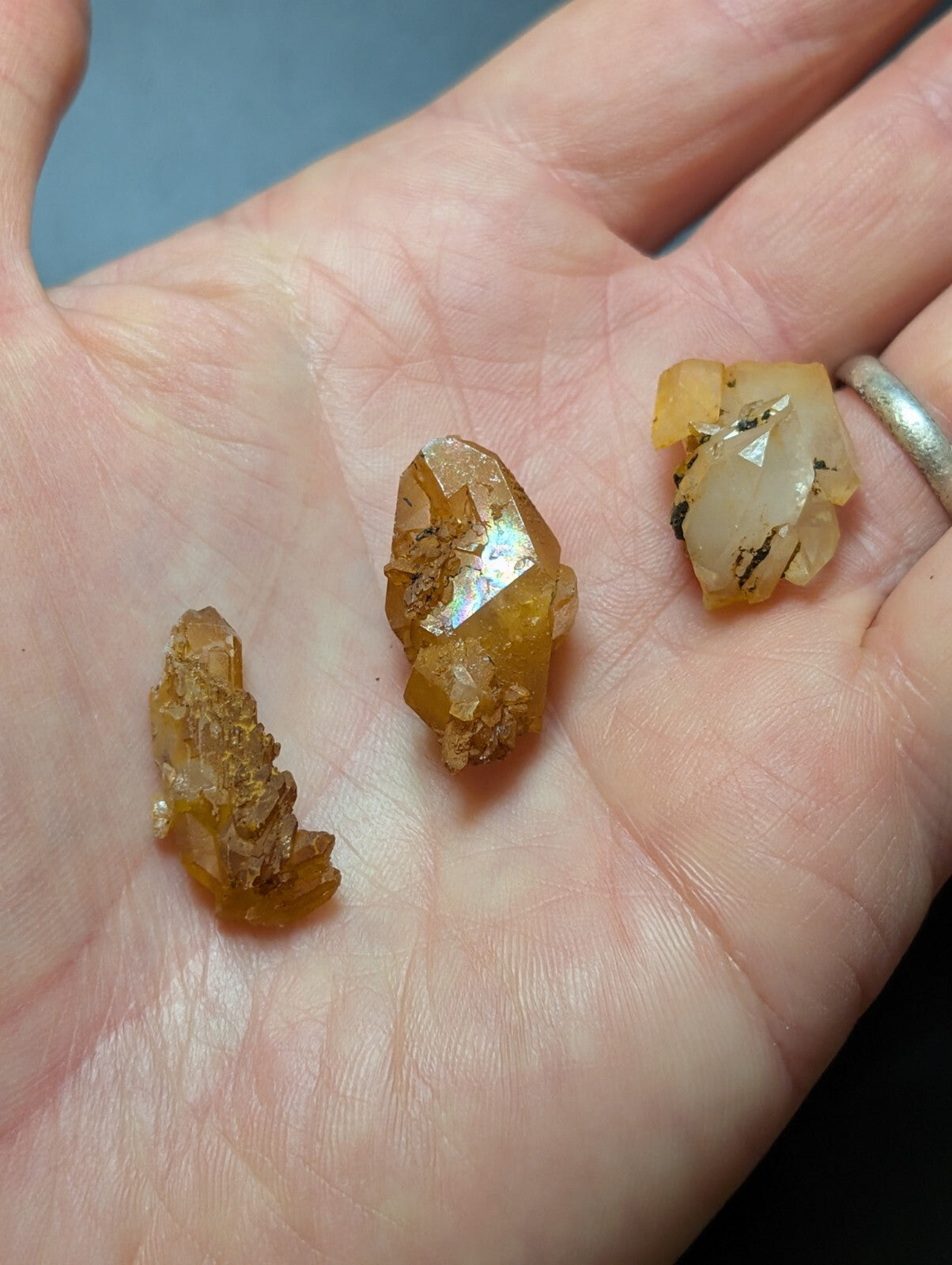 Three amber-colored, translucent mineral crystals with visible internal inclusions and rough, natural facets rest gently in an open palm.