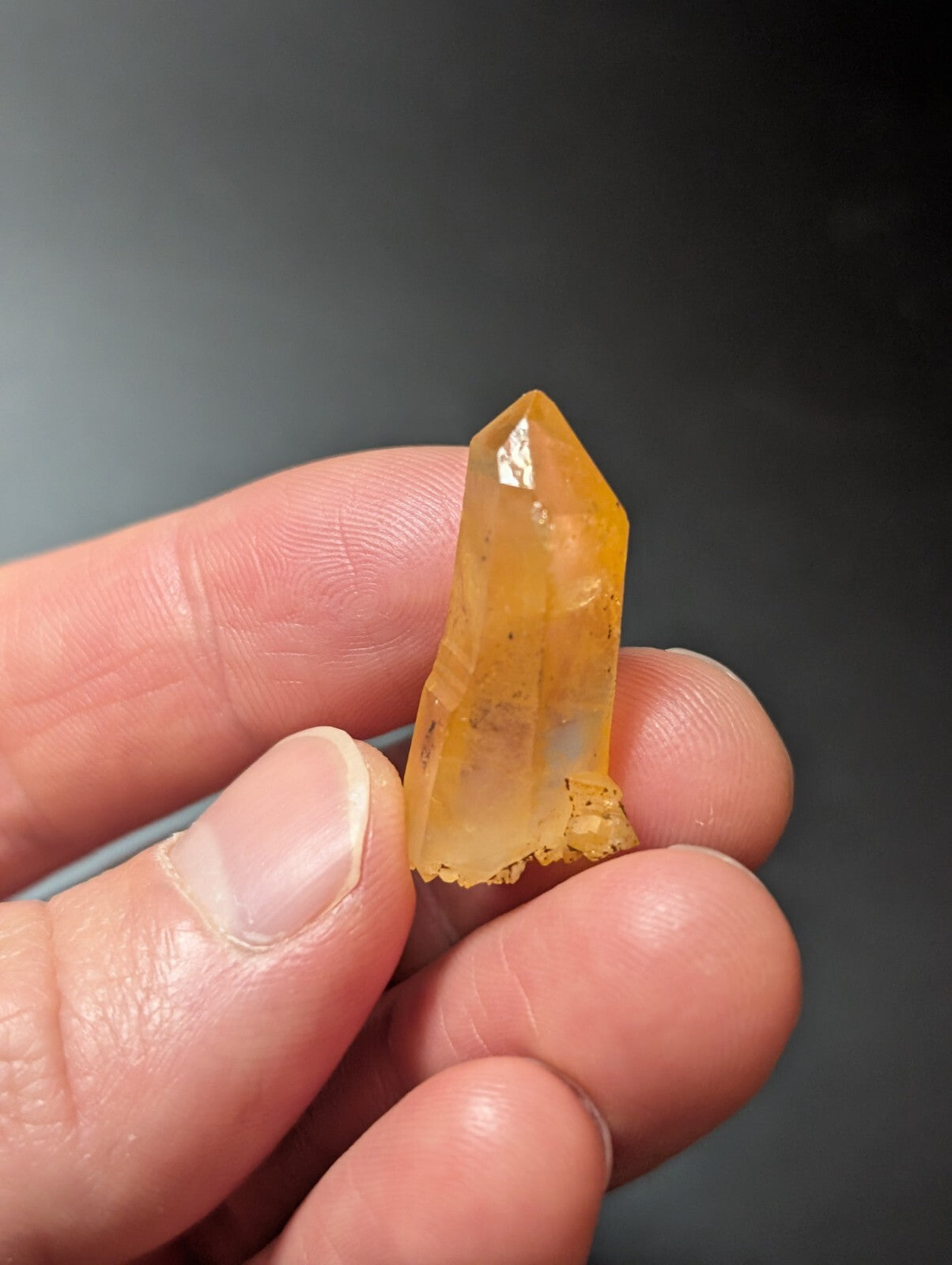 A translucent amber-colored quartz crystal with a pointed tip and natural inclusions, held gently between fingers.