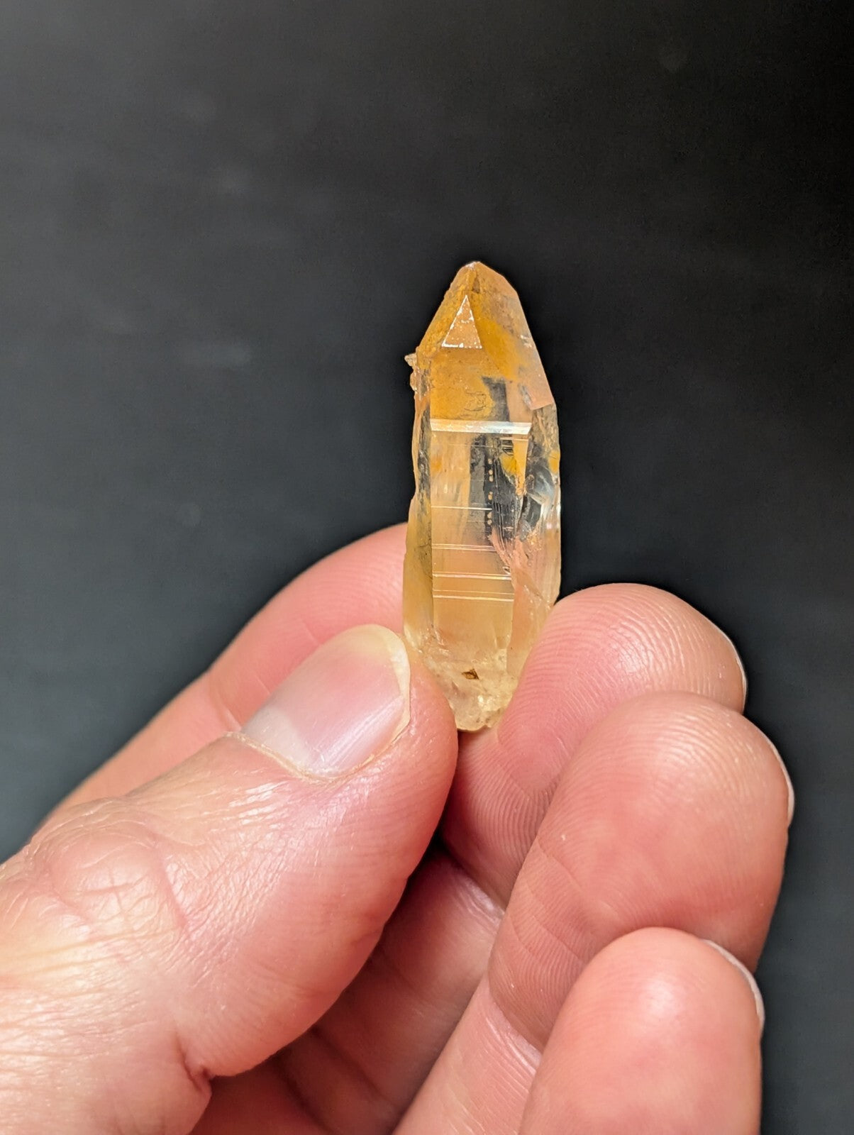 A translucent golden-yellow crystal with a pointed tip and visible internal striations, held gently between fingers.