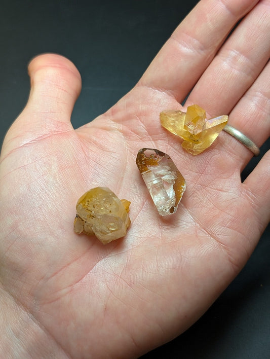 Three amber-hued, translucent crystal specimens with natural facets and earthy inclusions rest gently in an open palm.