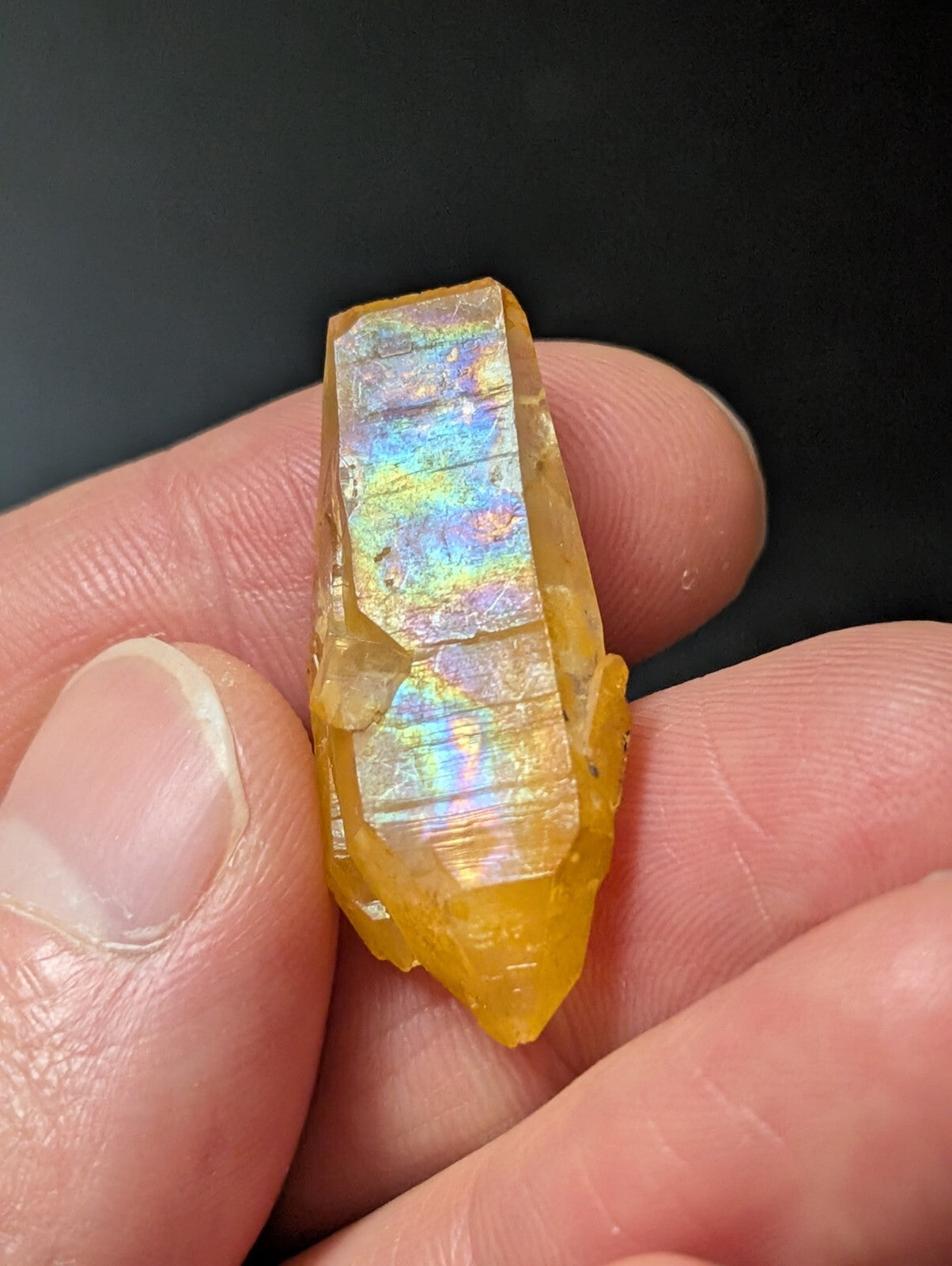 A translucent golden-yellow crystal with iridescent, rainbow-like facets held in a hand.