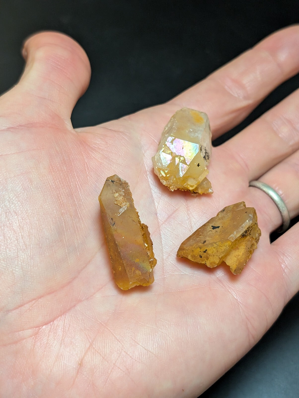 A hand holds three translucent amber-colored crystal specimens with natural facets and inclusions.