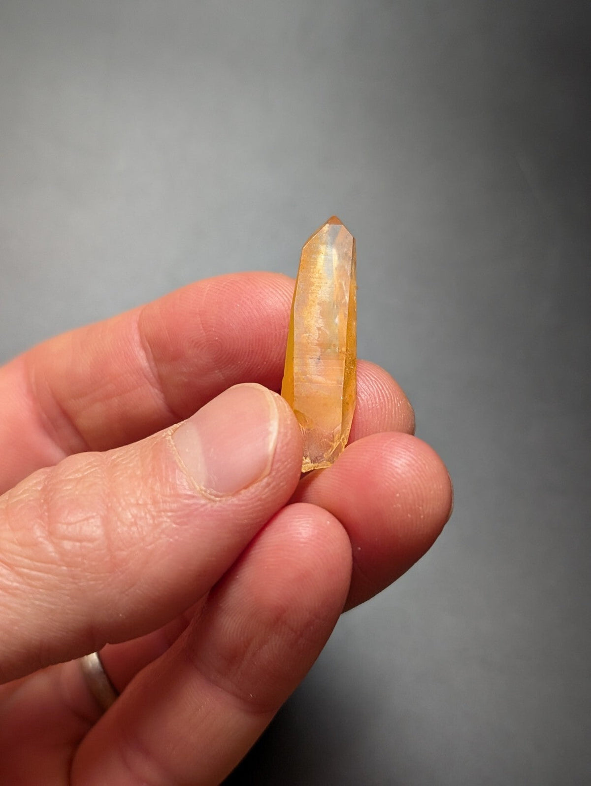A translucent golden-yellow citrine crystal point held gently in a hand.