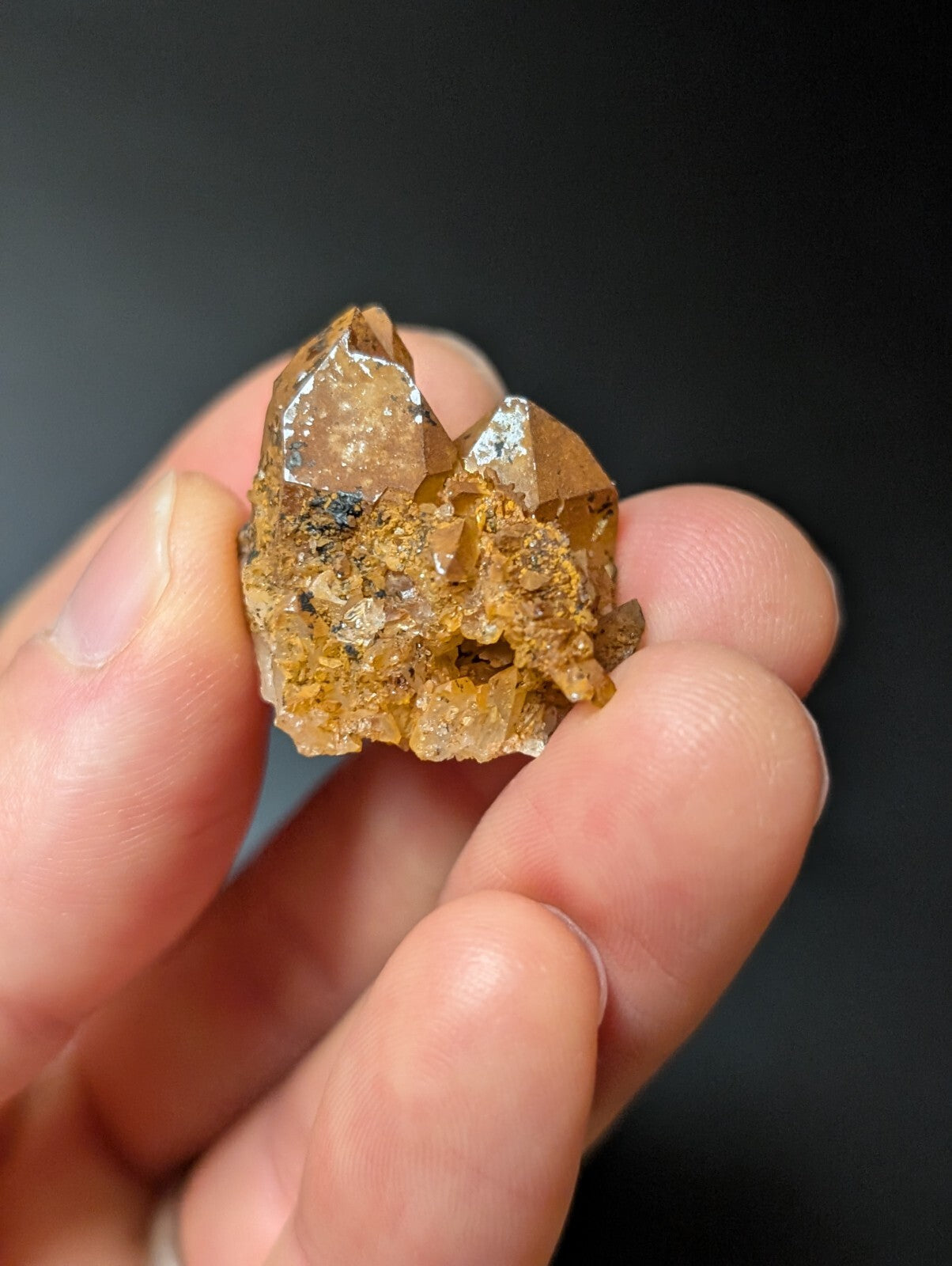 A translucent amber-colored crystal cluster with sharp, faceted points and a rough, earthy base.