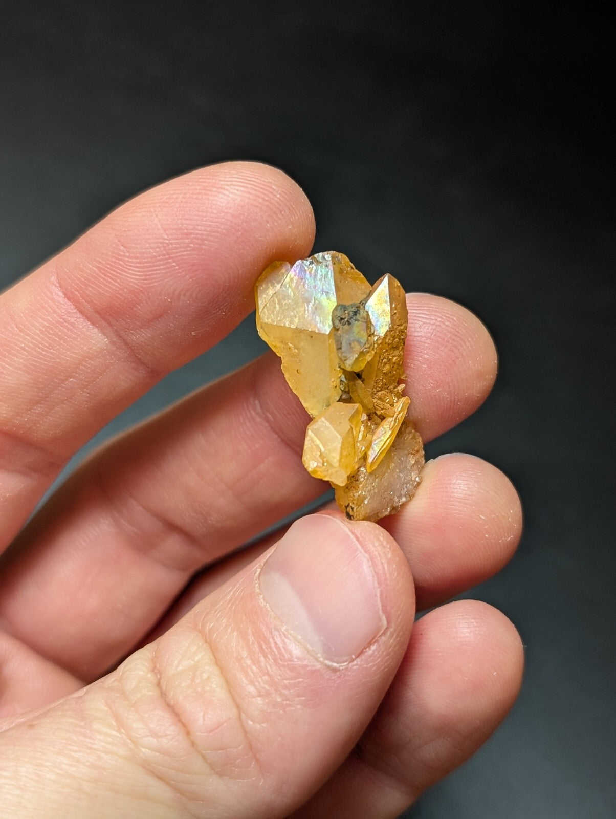 A cluster of golden-yellow, faceted crystals with iridescent highlights held gently between fingers.