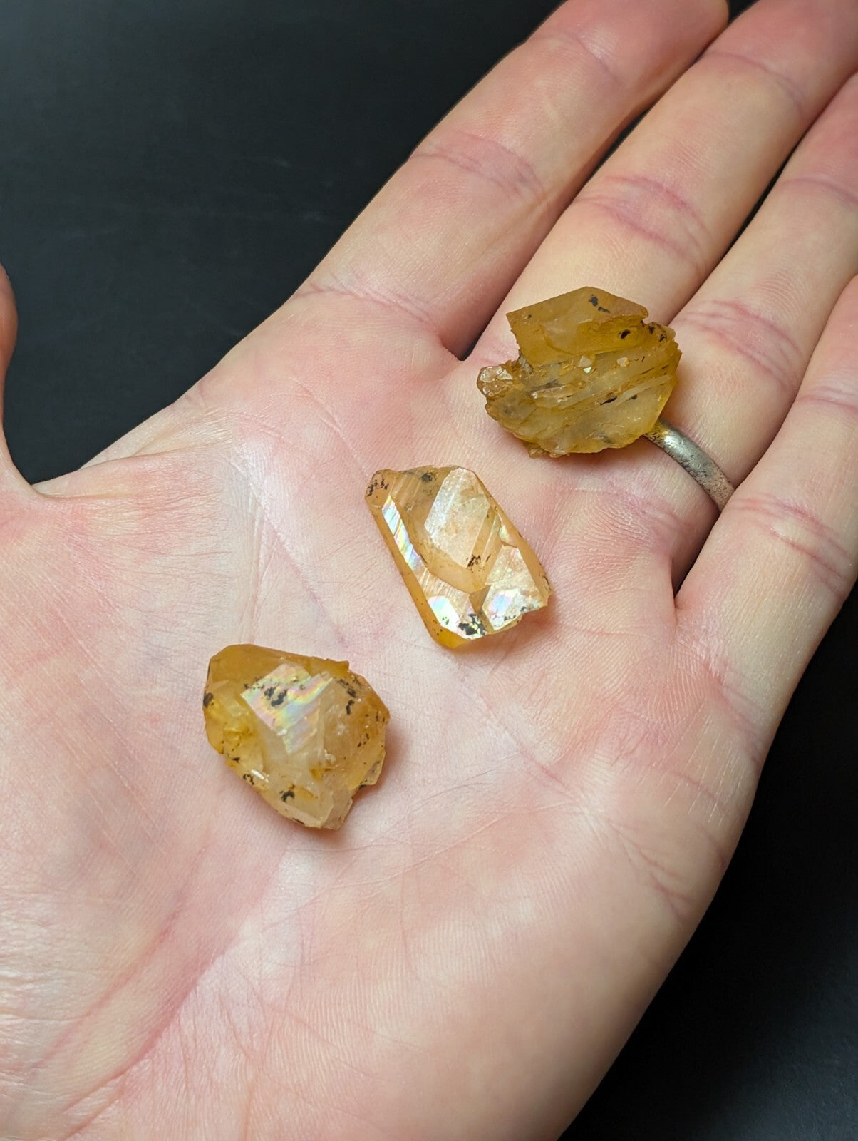 Three rough, amber-hued citrine crystals with natural facets and inclusions rest gently in an open palm.
