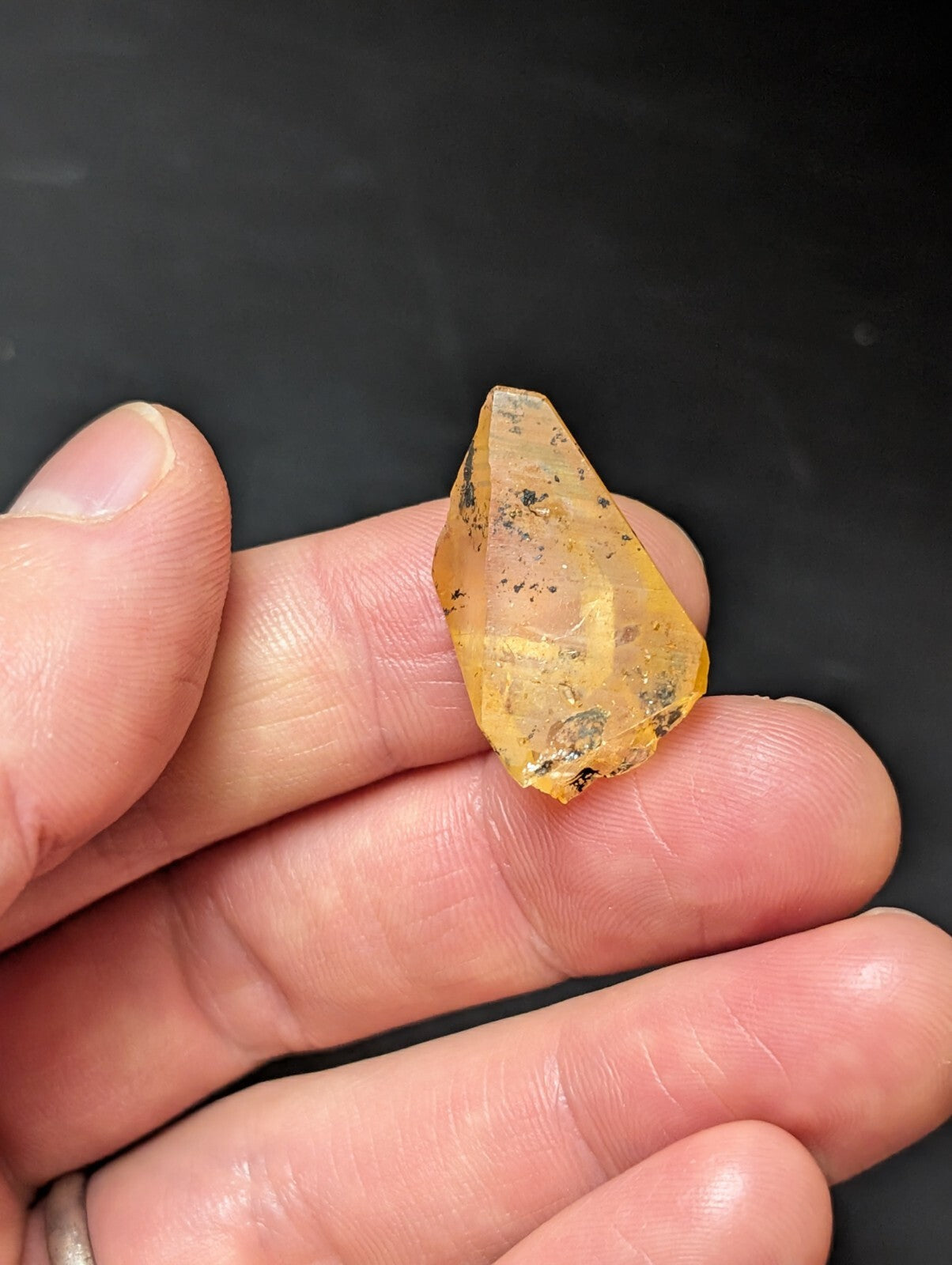A translucent yellow crystal with natural inclusions and a pointed, faceted shape.
