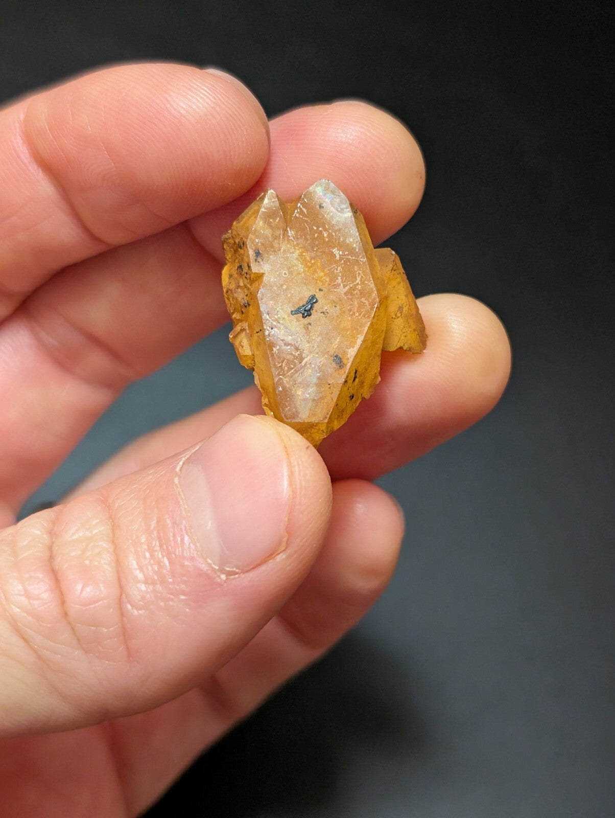 A translucent yellow-orange crystal with a faceted, geometric shape and some darker inclusions.