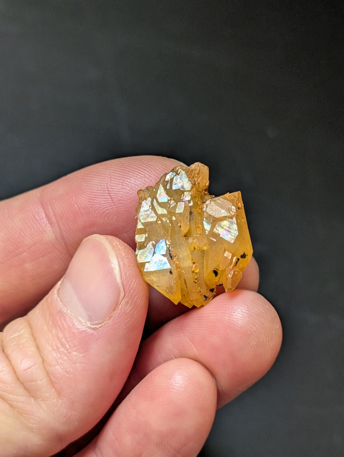 A translucent amber-colored crystal cluster with iridescent facets and small dark inclusions.