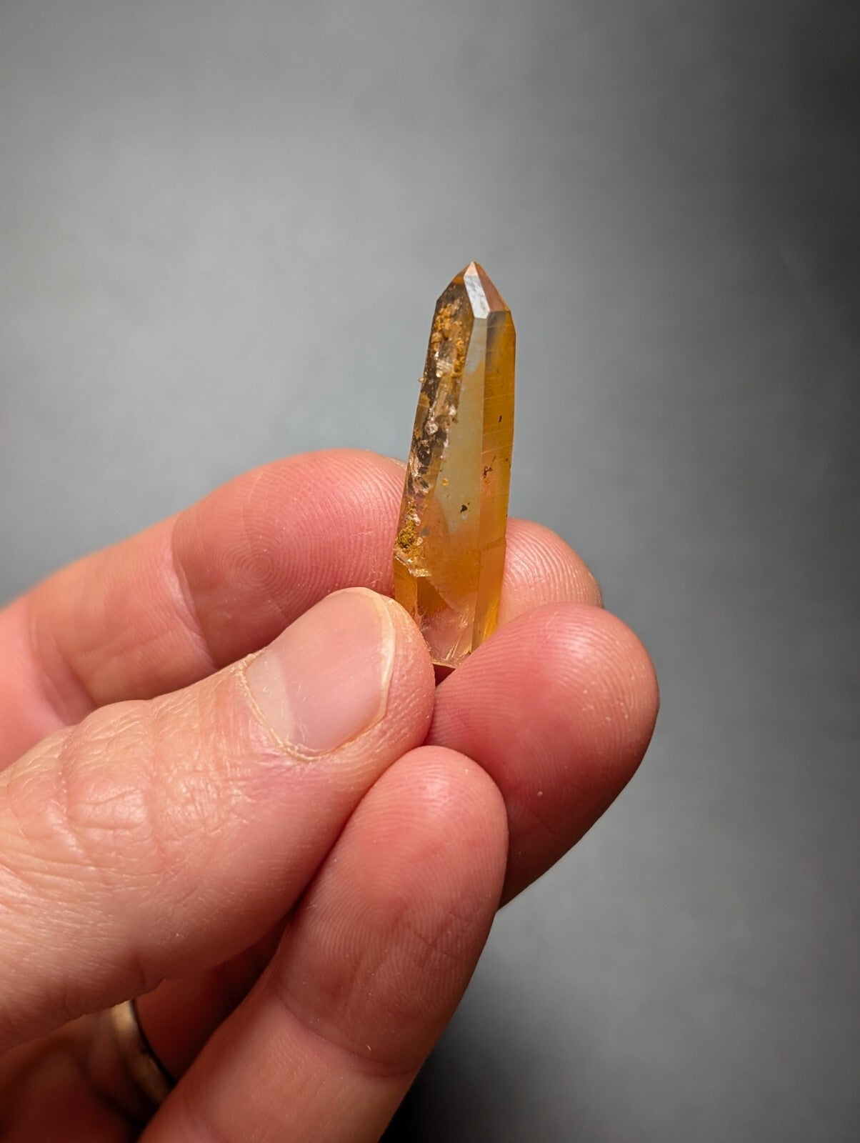 A translucent amber-colored quartz crystal with golden inclusions, held delicately between fingers.