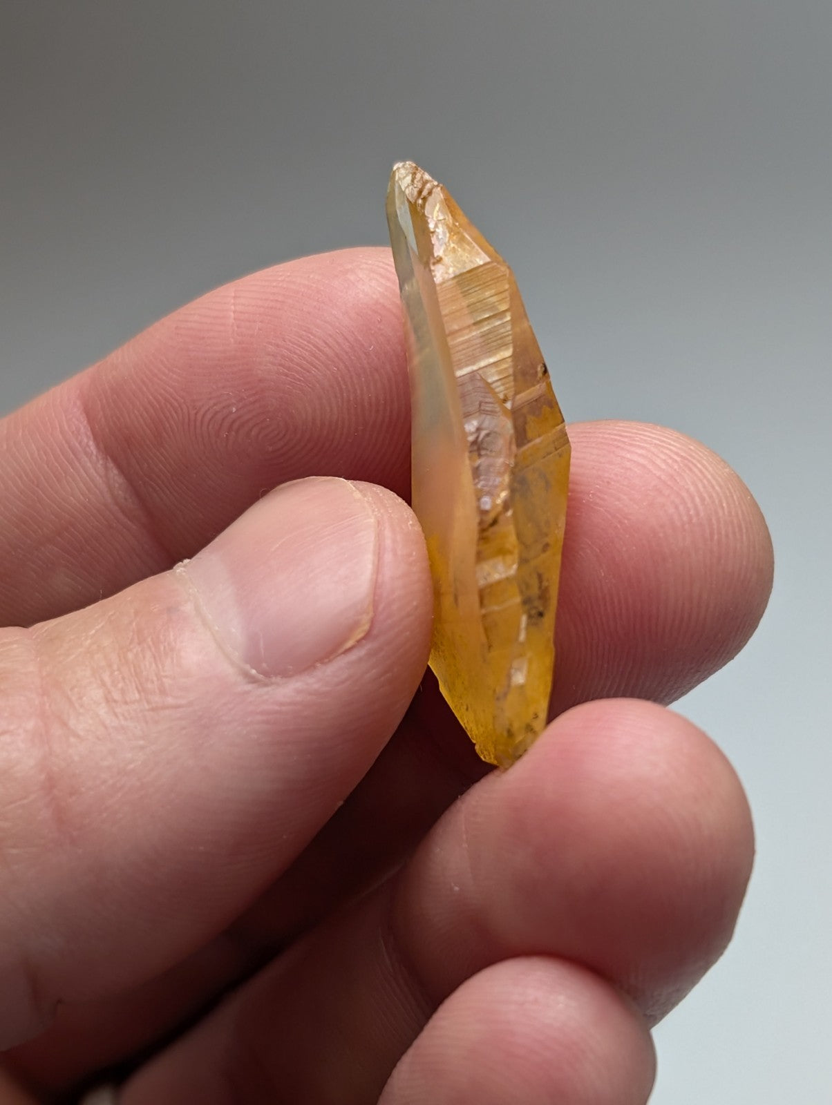 A translucent yellow arkansas quartz crystal with natural iridescence and internal striations held between fingers
