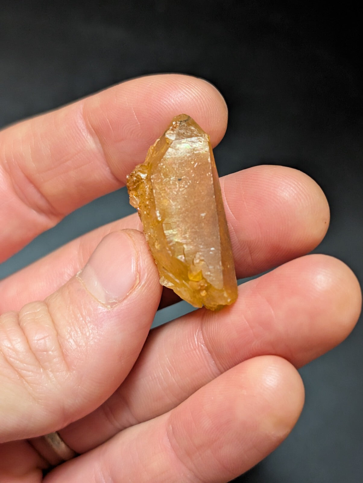 A translucent golden-yellow crystal with a pointed tip and natural facets, held gently in someone’s hand.