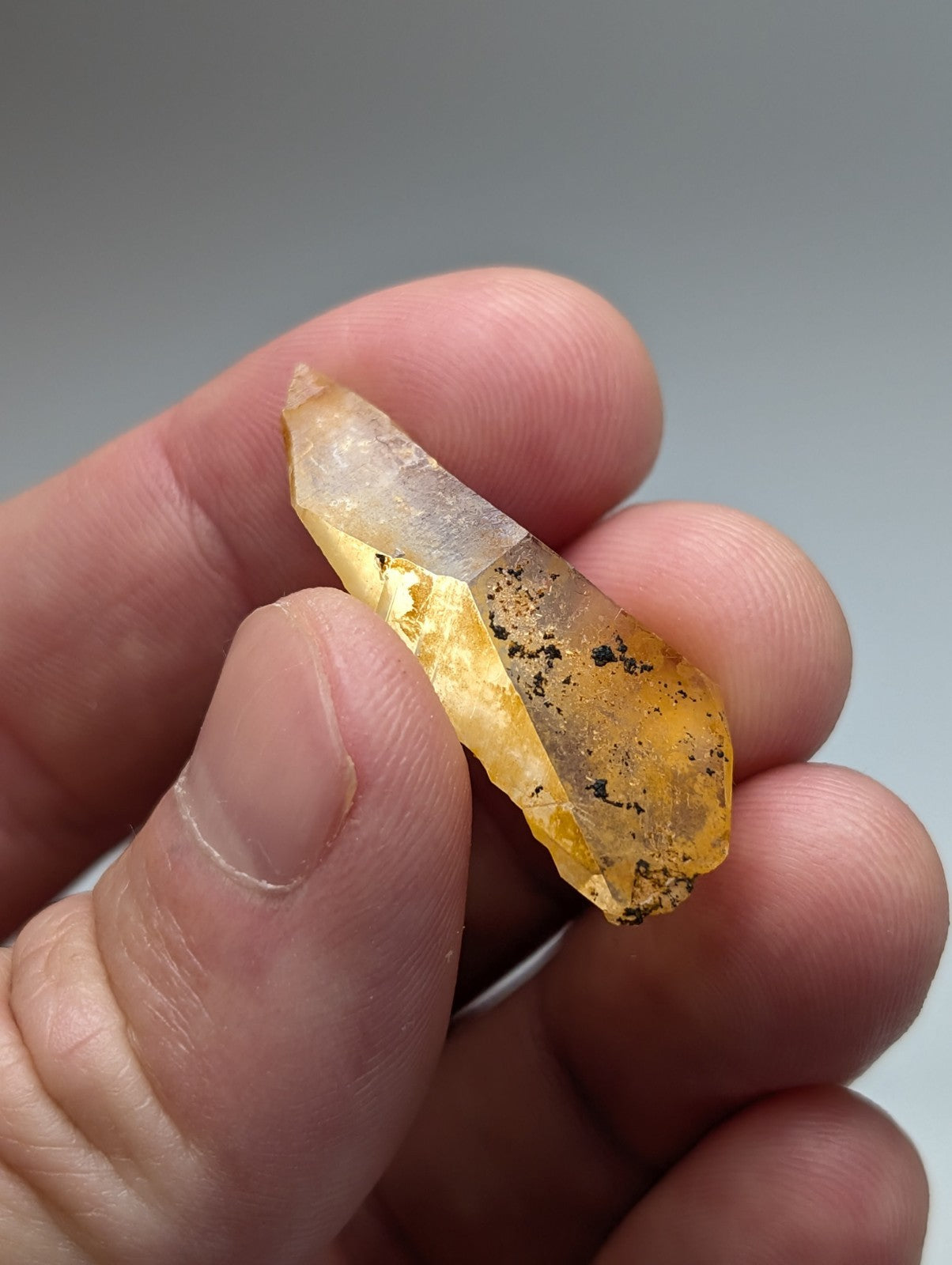 A translucent golden-yellow Arkansas quartz crystal with natural iridescence and inclusions held between fingers