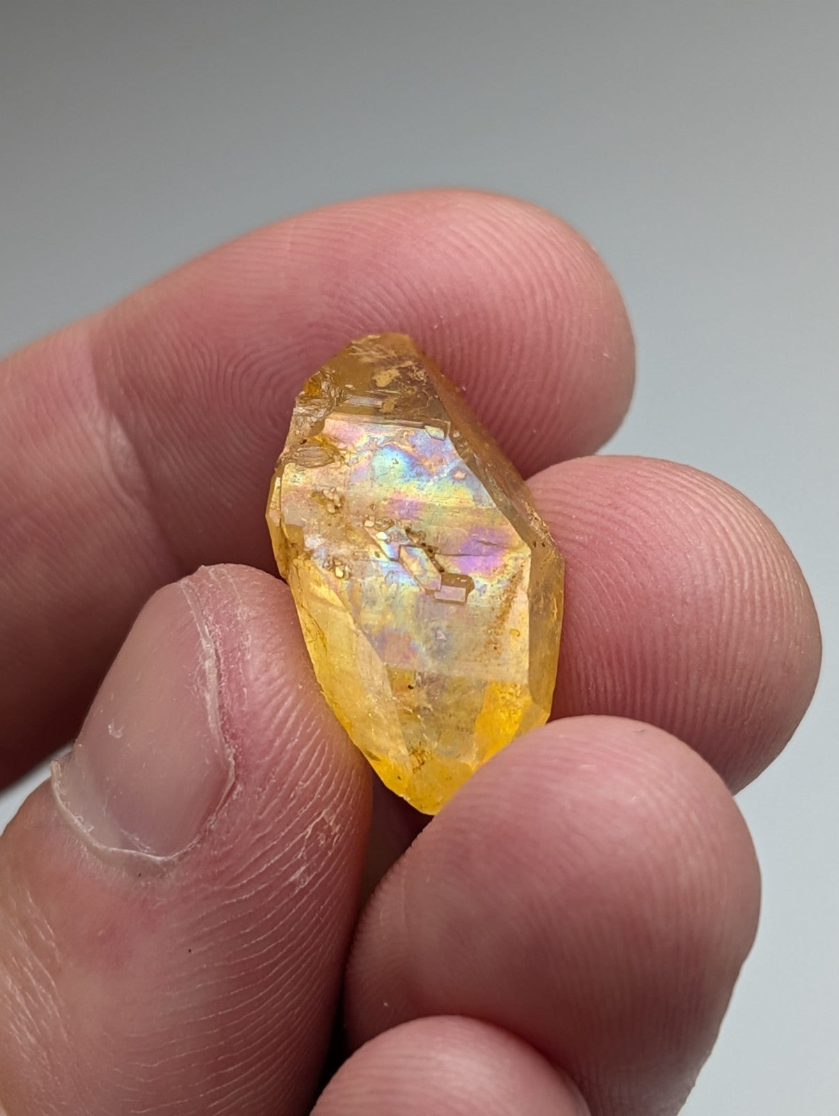 A translucent golden-yellow arkansas quartz crystal with natural iridescence held between fingers in a set of 3