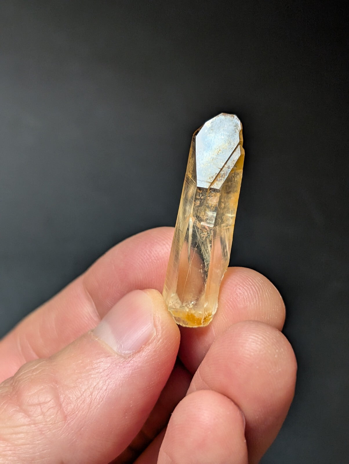 A translucent yellow crystal with a pointed, faceted top and natural mineral inclusions.