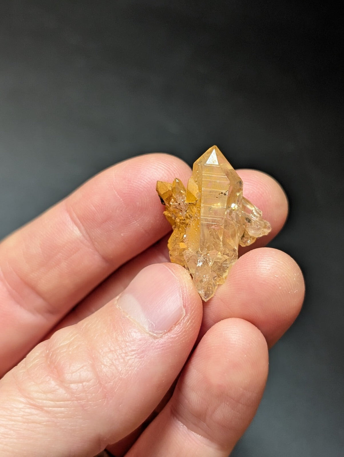 A translucent golden-yellow crystal cluster with a pointed, faceted central spike and smaller branching crystals.