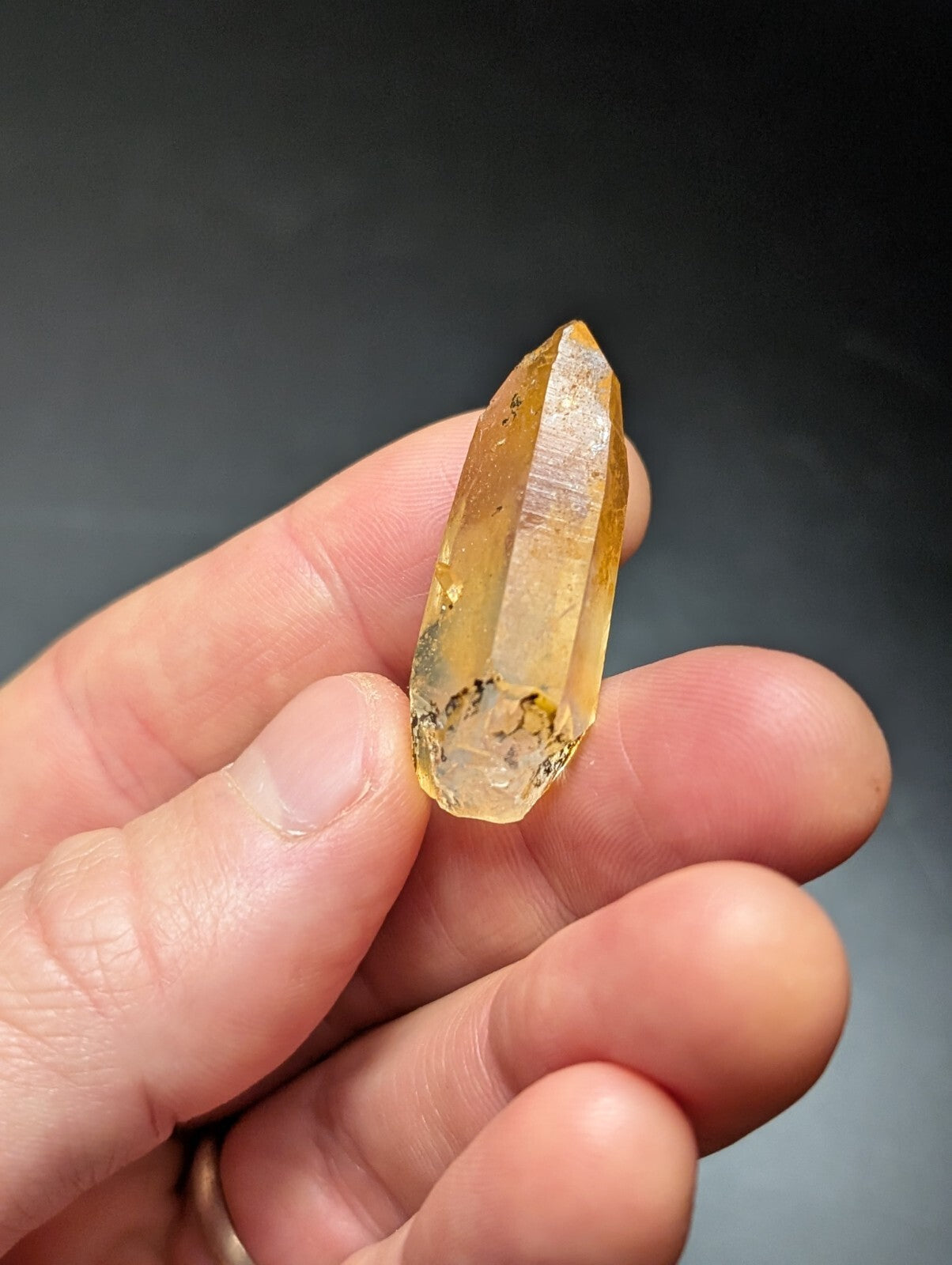 A translucent golden-yellow citrine crystal with a pointed tip and natural inclusions, held gently between fingers.