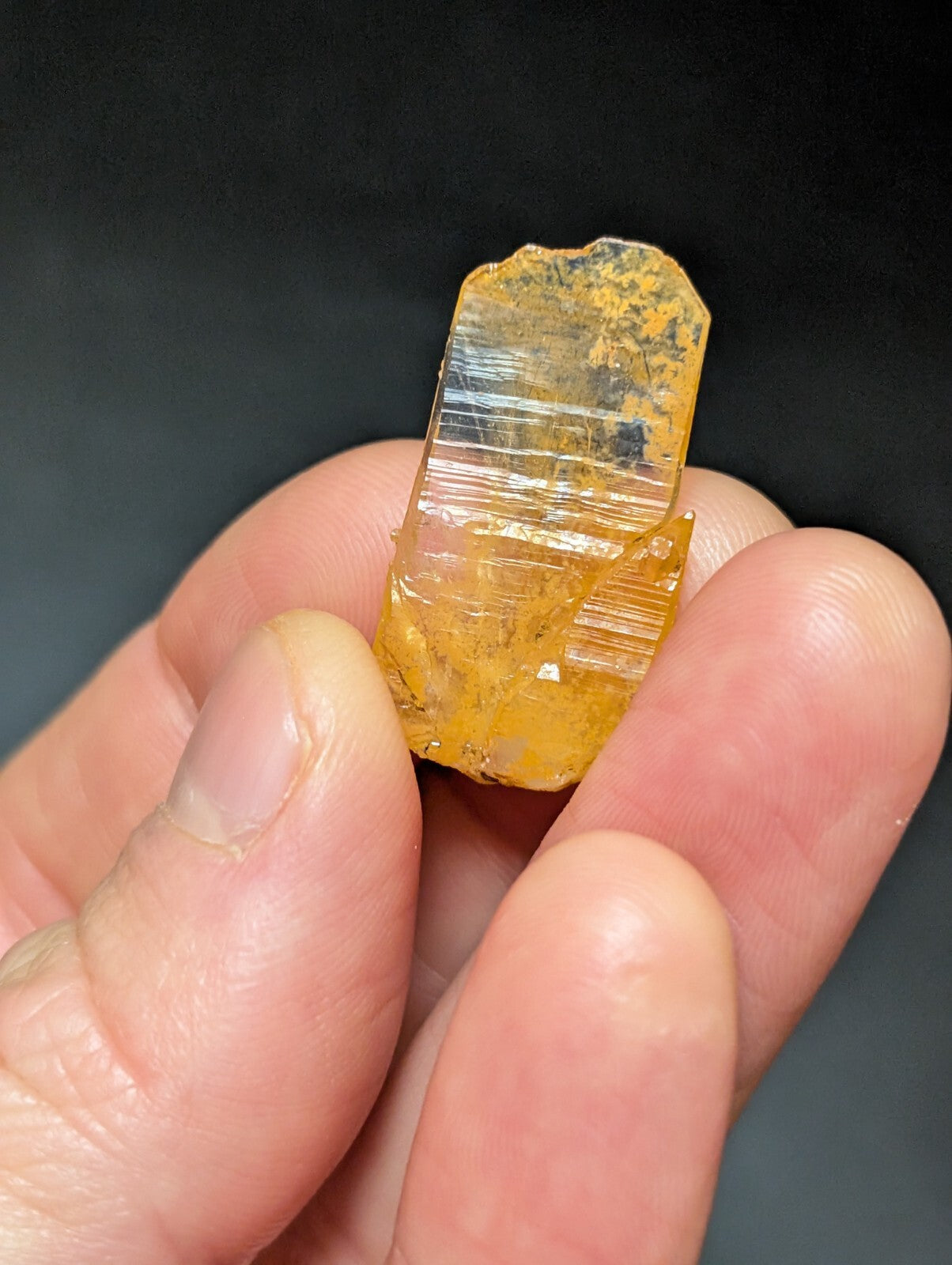 A translucent amber-colored mineral specimen with visible striations and a rough, natural edge.
