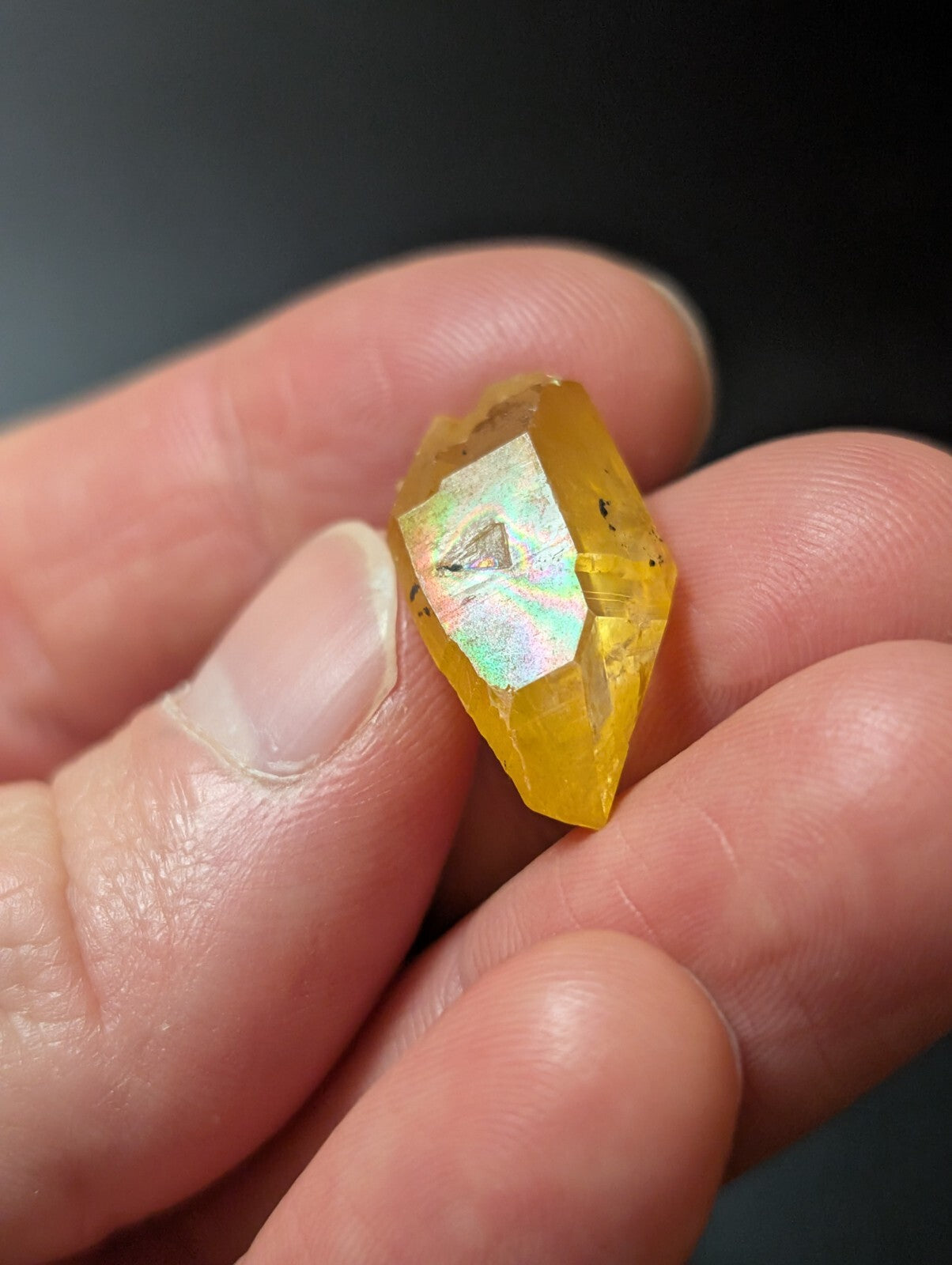 A translucent yellow crystal with a faceted, geometric shape and subtle iridescent flashes.