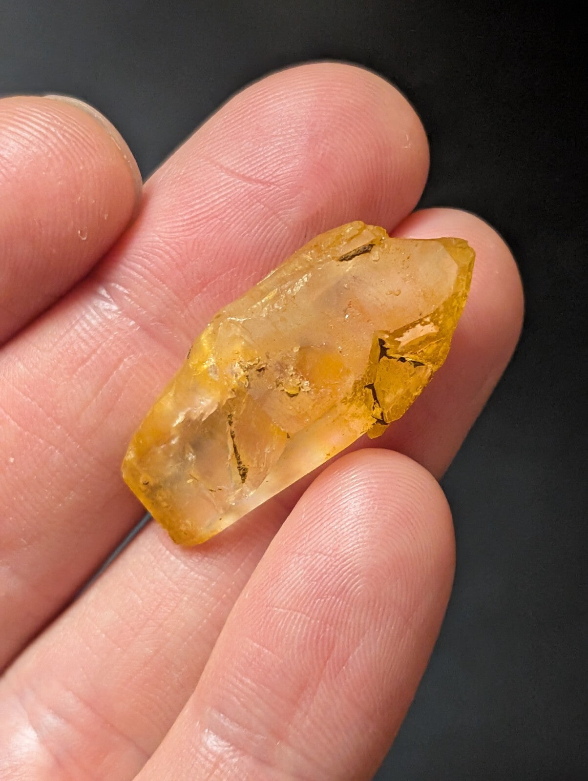 A translucent yellow crystal with natural facets and internal inclusions, held gently between fingers.
