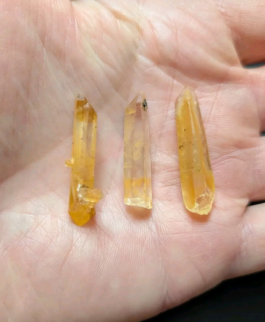 Three translucent yellow citrine crystals with natural inclusions, held gently in an open palm.