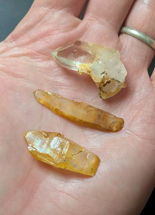 A hand holds three translucent, amber-hued crystal points with natural facets and earthy inclusions.