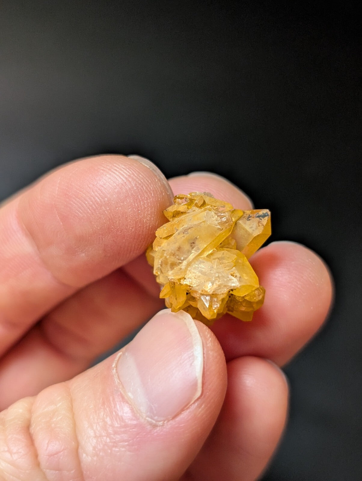 A cluster of translucent yellow crystals with sharp, angular facets held gently between fingers.
