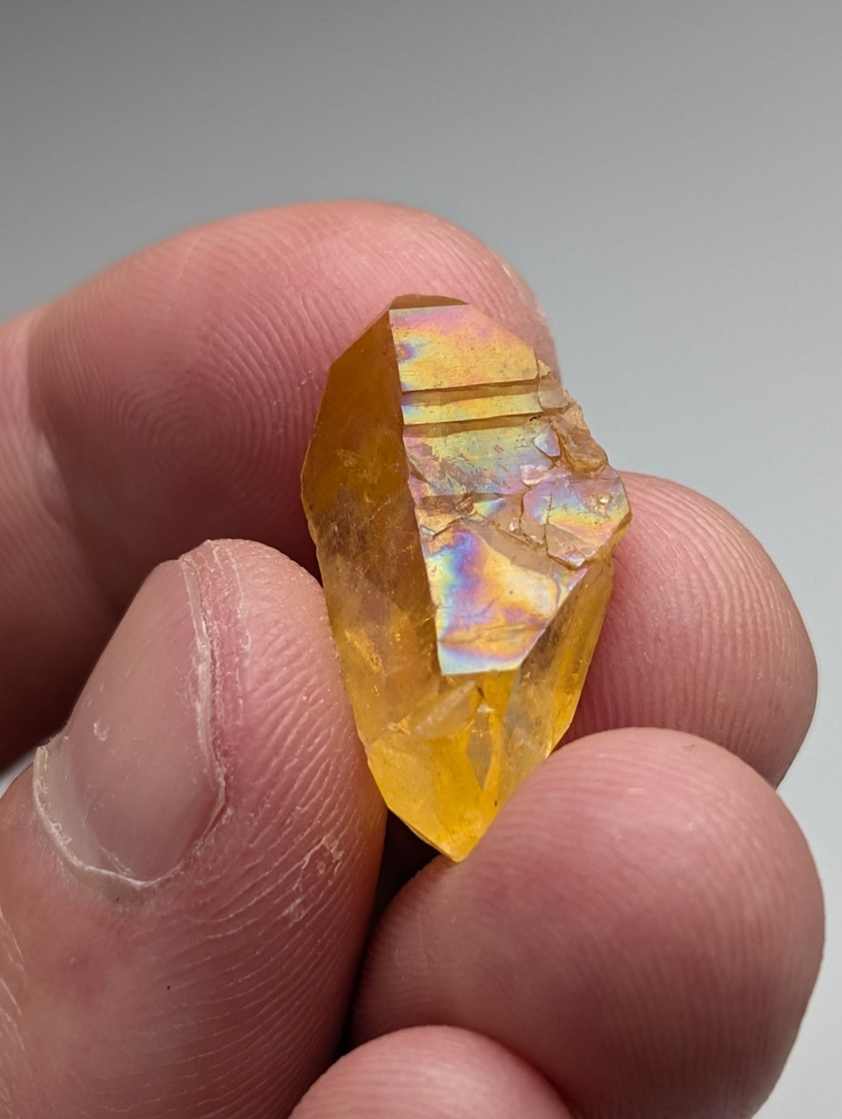 A translucent golden-yellow Arkansas quartz crystal with natural iridescence and rainbow reflections on its facets