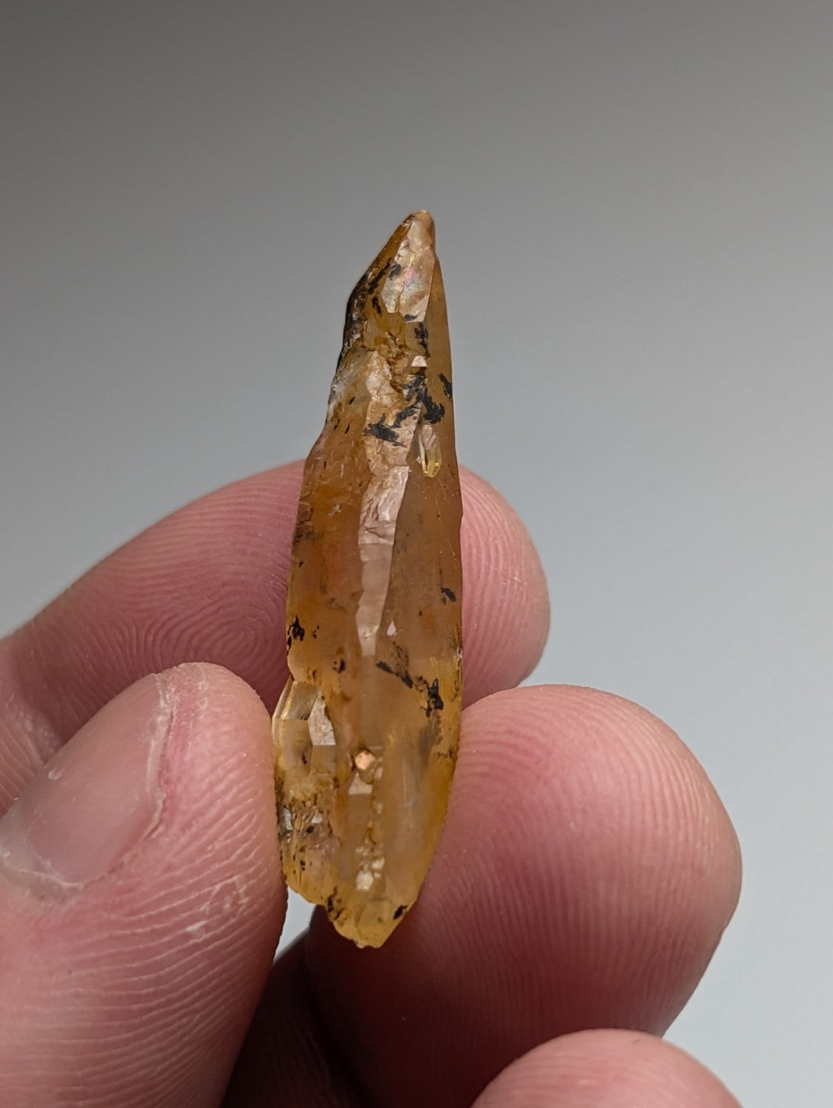 A translucent amber Arkansas quartz crystal with natural iridescence and dark inclusions held between fingers