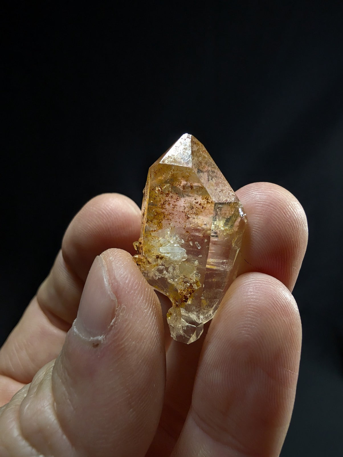 A translucent golden-yellow citrine crystal with a pointed tip and natural inclusions, held gently between fingers.