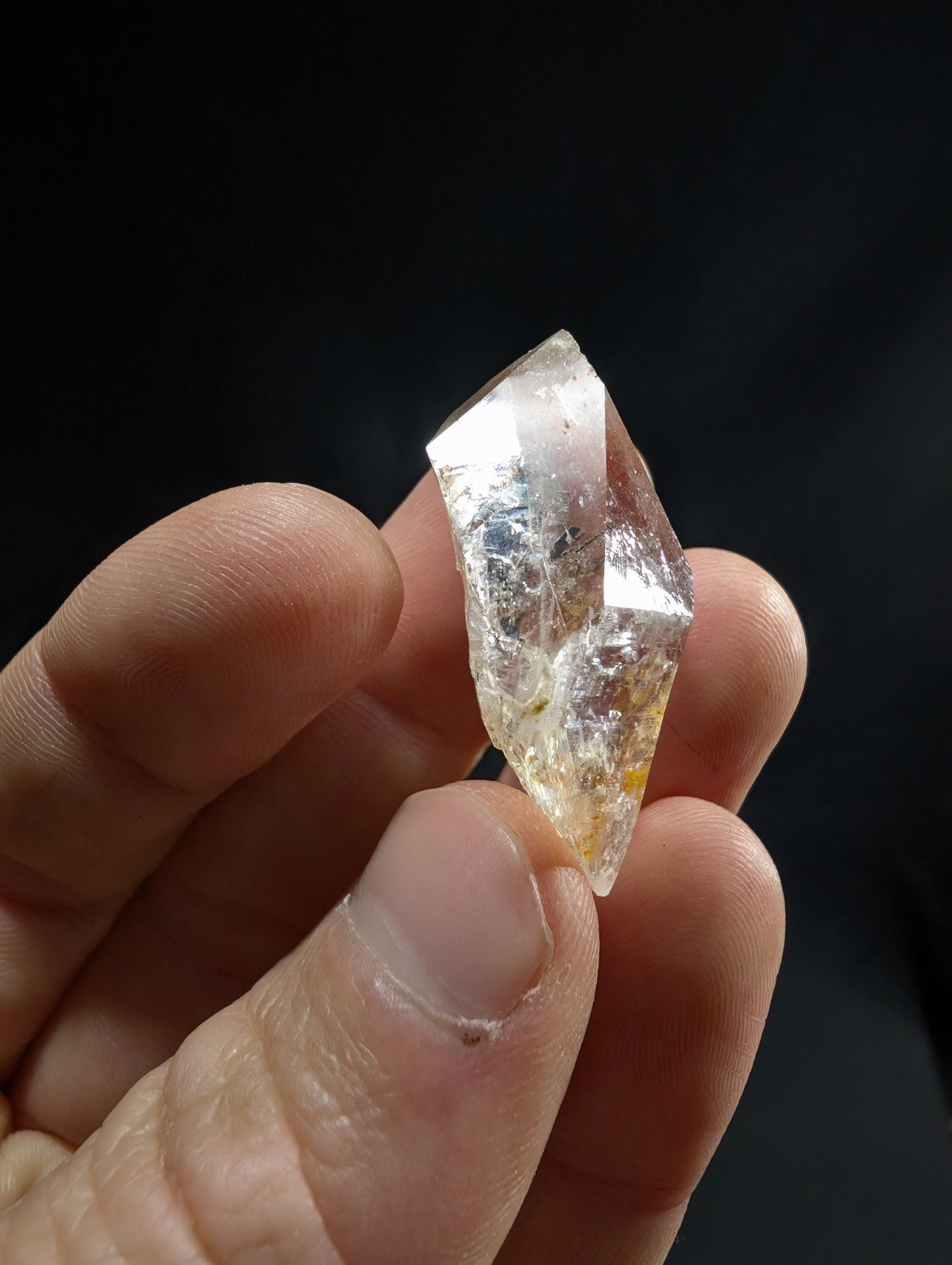 A translucent, clear quartz crystal with subtle golden inclusions and sharp geometric facets.