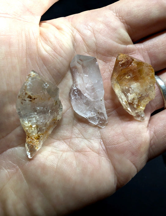 Three raw quartz crystals, featuring clear to golden hues and natural facets.