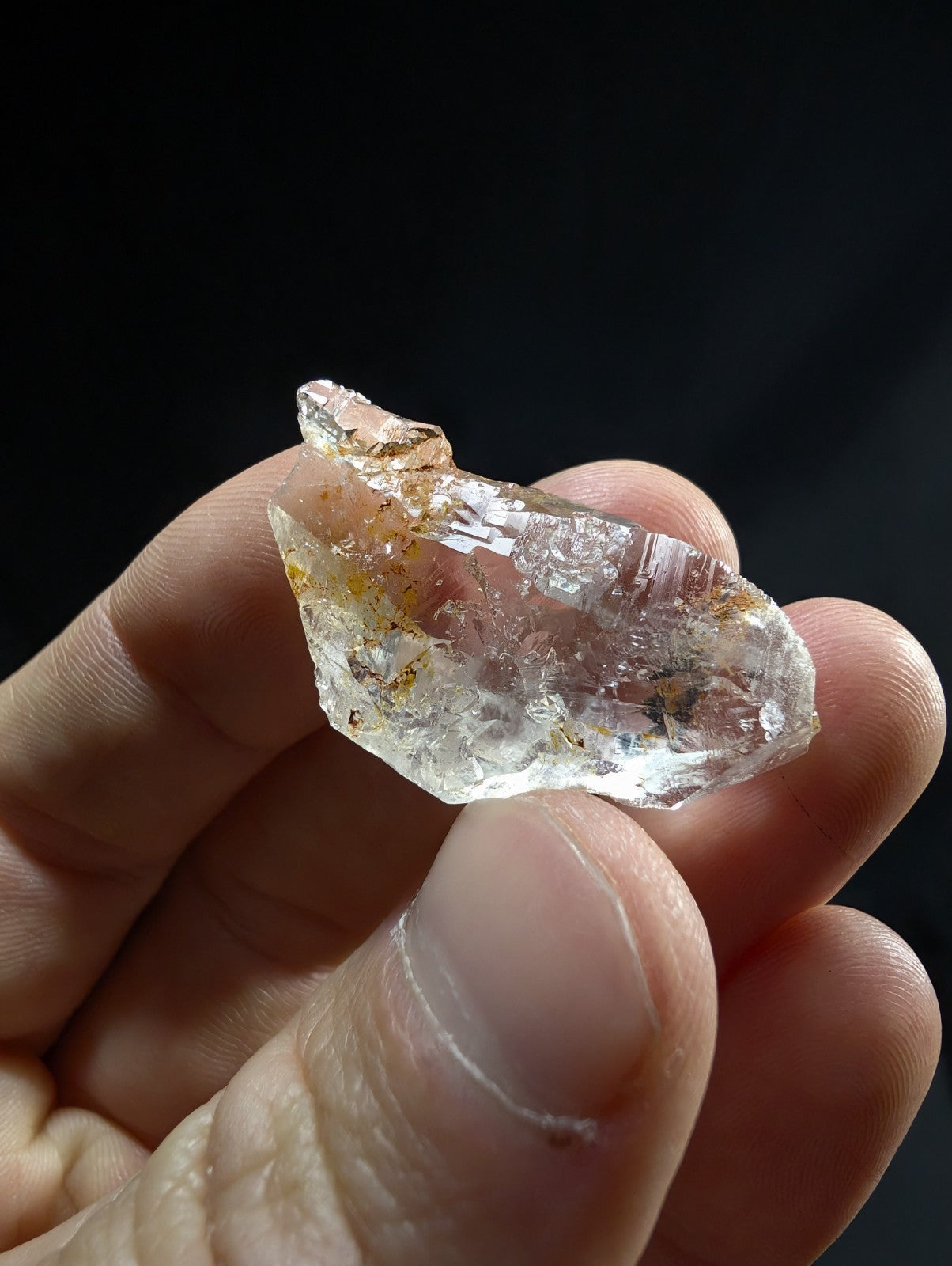 A translucent, clear quartz crystal with subtle golden inclusions and a rough, natural faceted surface.