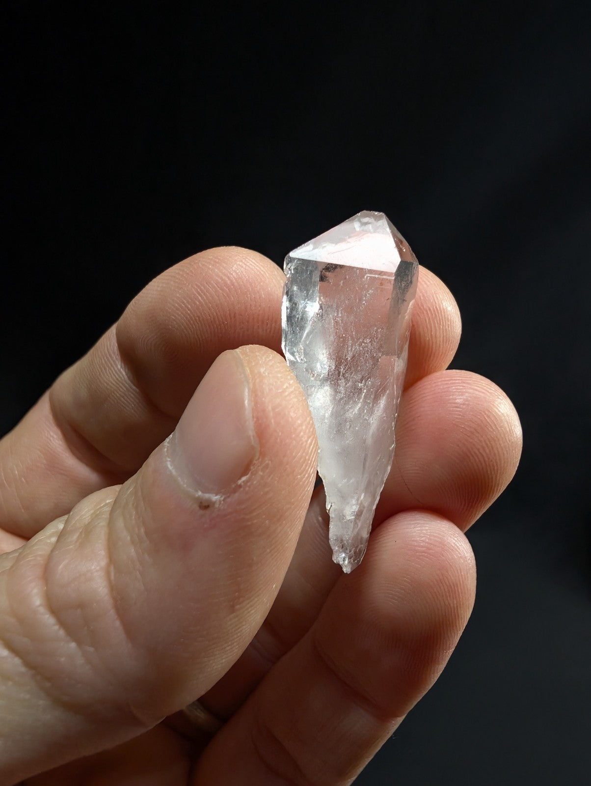 A translucent, clear quartz crystal with a pointed tip and faceted surface.