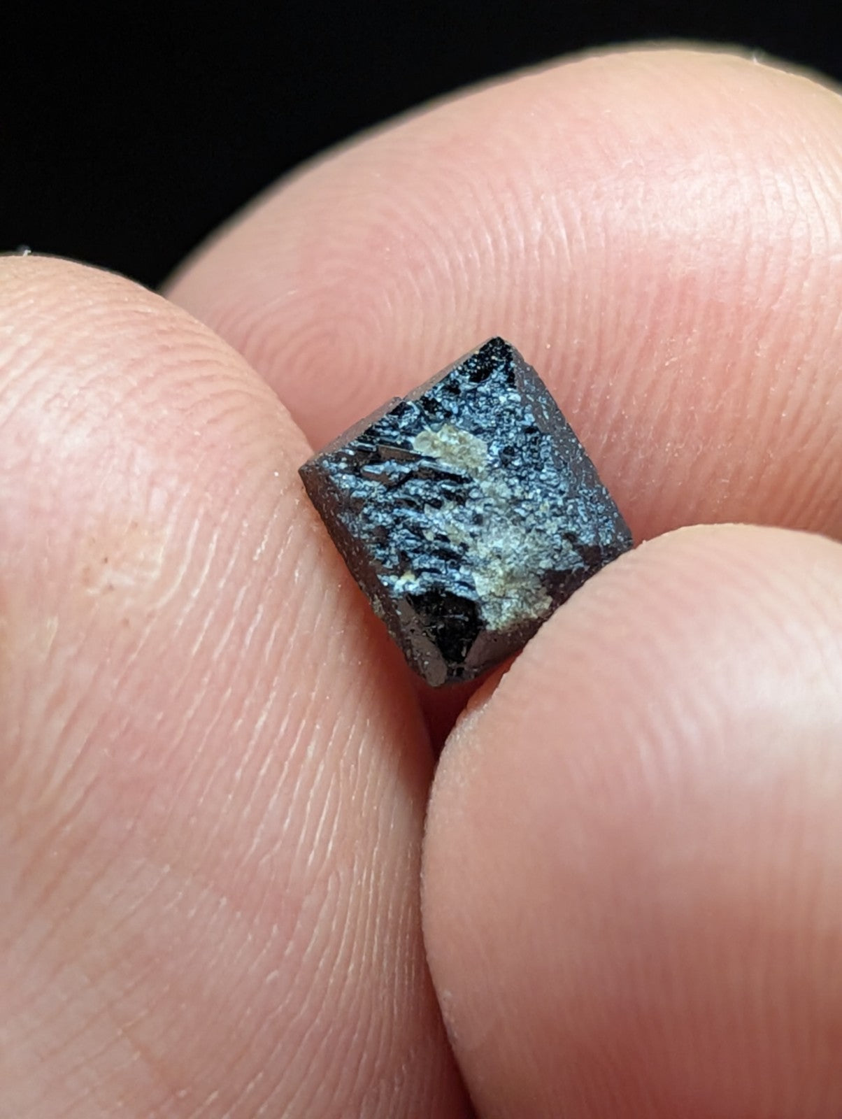 A dark, square-cut mineral specimen with a rough, textured surface and subtle lighter patches.