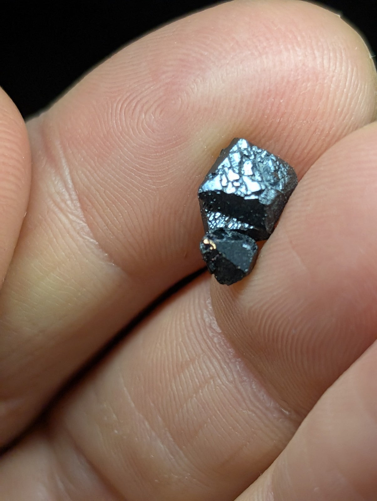 A small, dark metallic mineral specimen with a rough, faceted surface and subtle iridescent sheen.