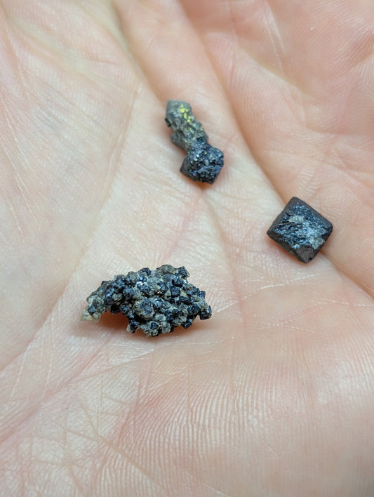 Three dark, irregularly shaped mineral specimens rest in the palm of a hand.
