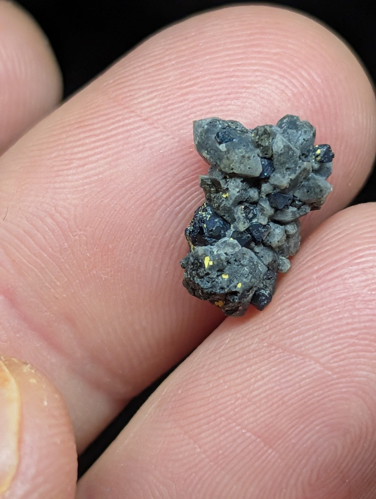 A dark gray, rough-textured mineral specimen with small yellow flecks and jagged crystalline formations.