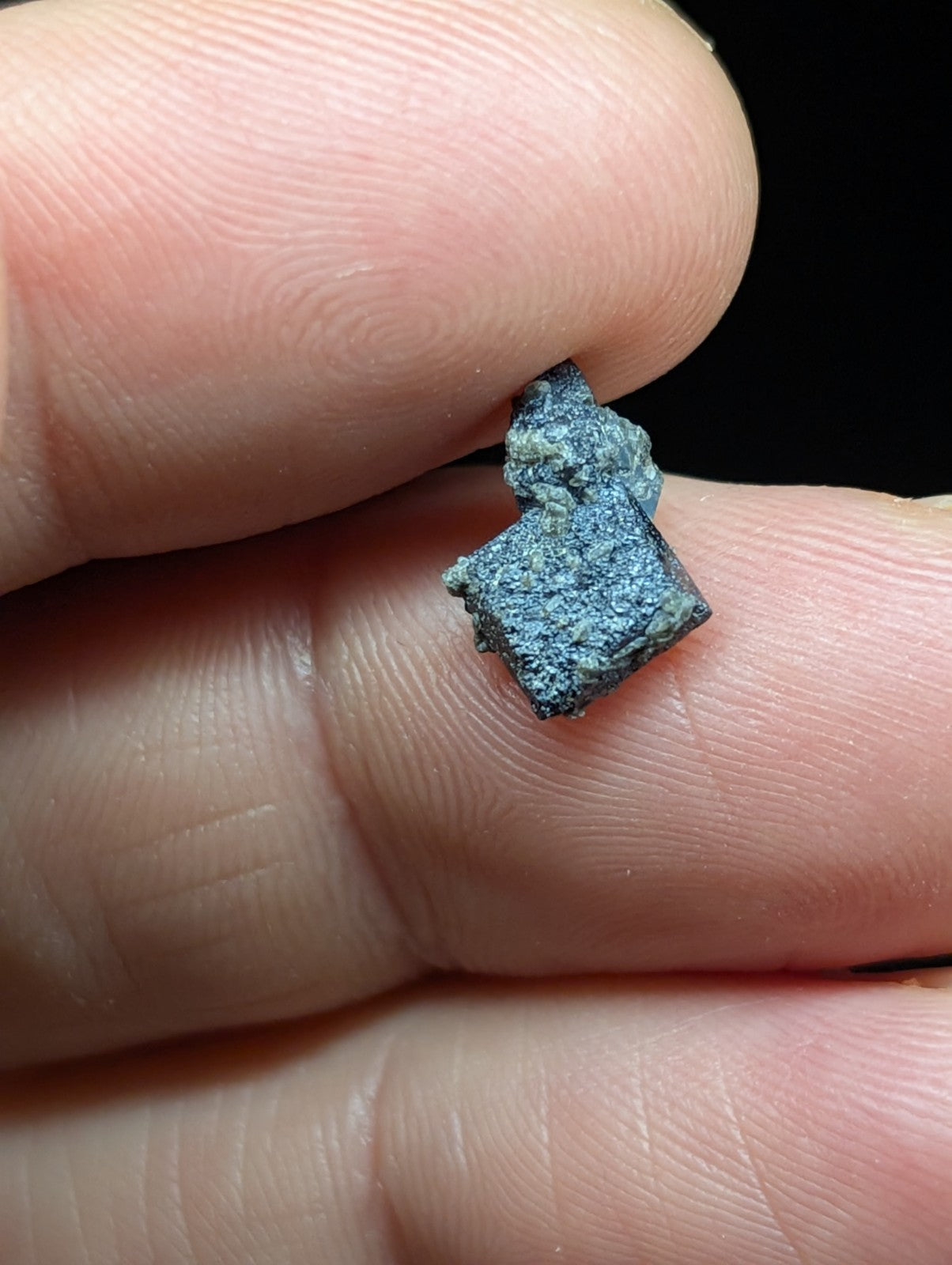 A small, irregularly shaped metallic fragment with a dark blue-green patina and rough texture.