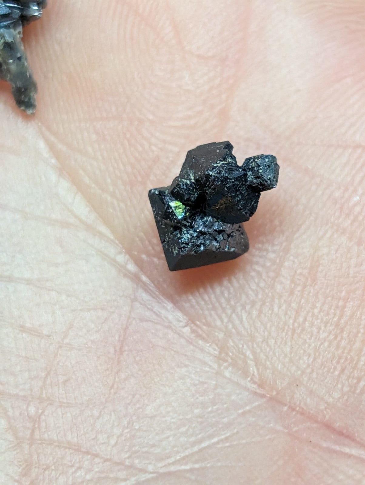 A small, irregularly shaped black mineral specimen with a rough, jagged surface and faint greenish highlights.