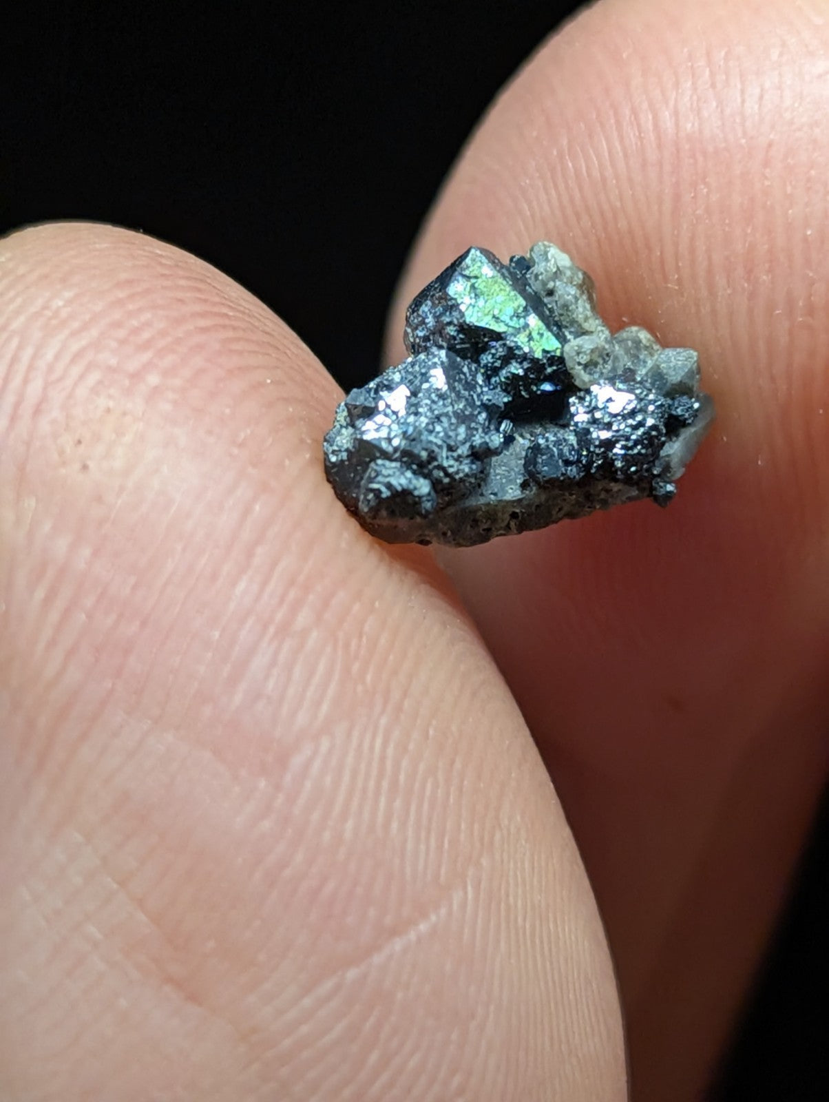 A small, iridescent green and black mineral specimen with a rough, crystalline texture.